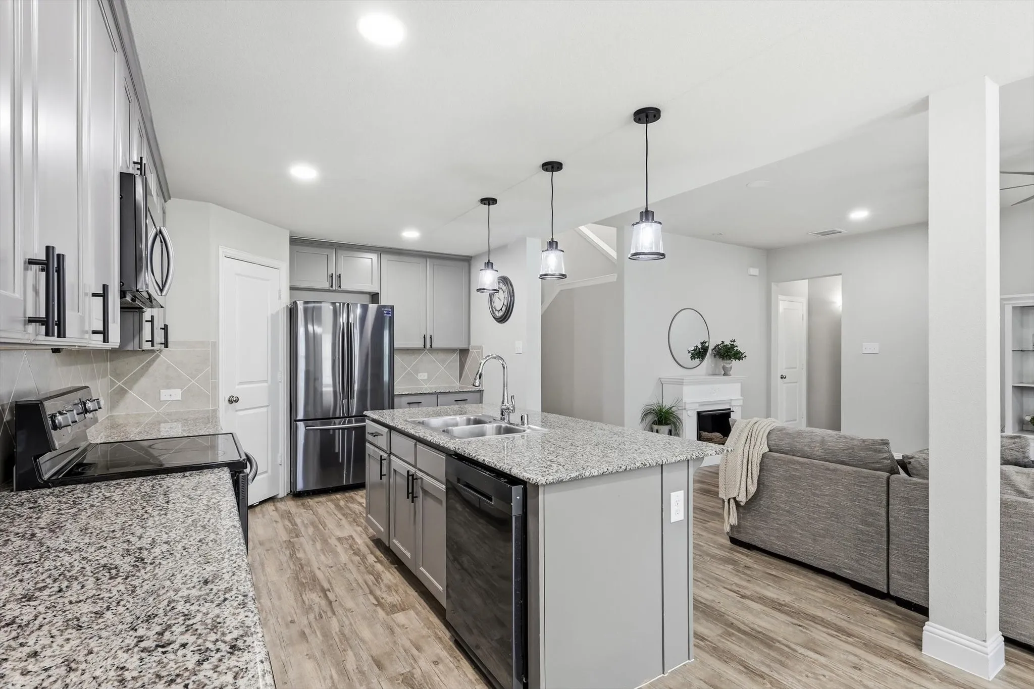 Open-concept kitchen featuring granite countertops, stainless steel appliances, a central island with pendant lighting, and wood-finish flooring