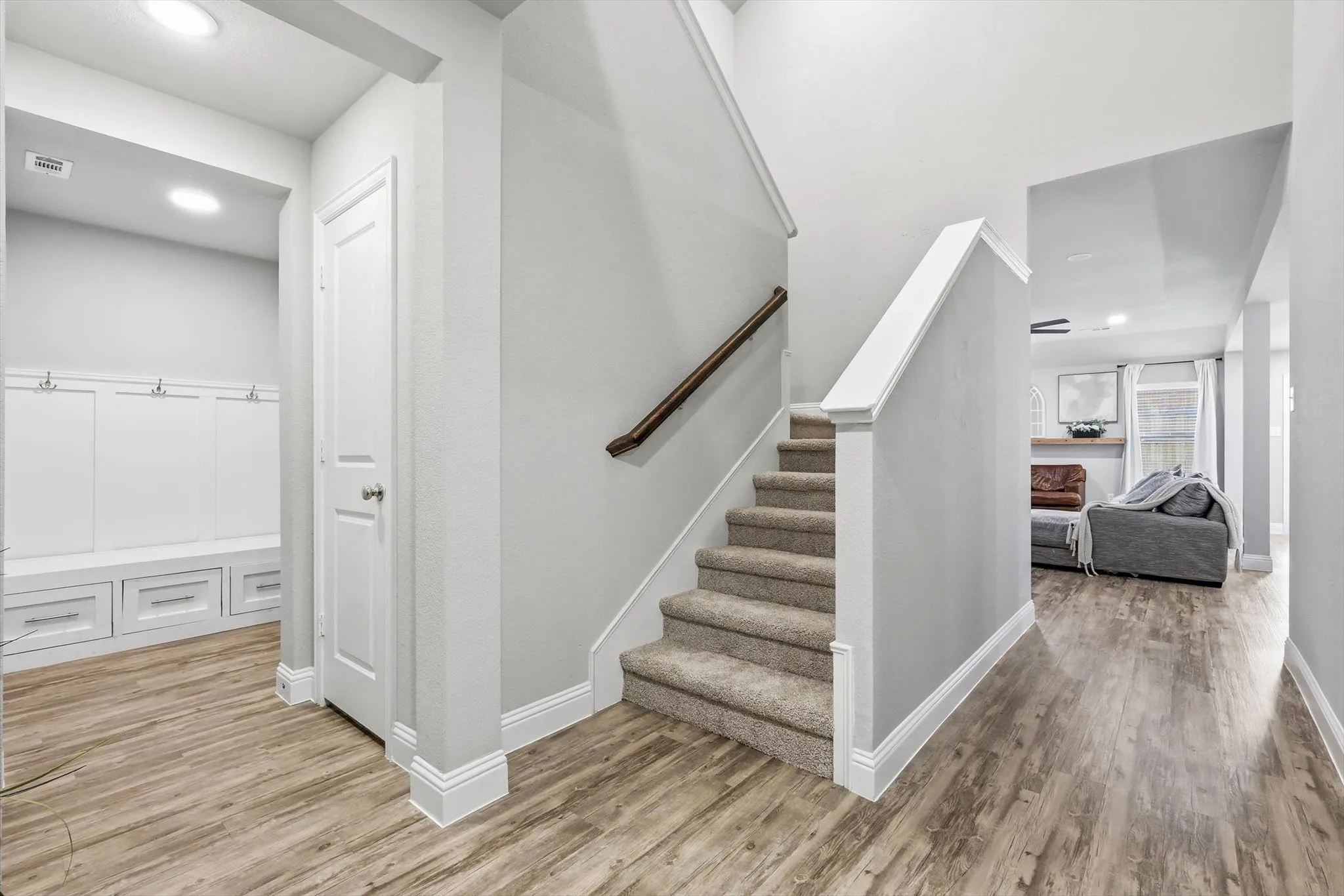 Interior entryway with wood-finish flooring, a carpeted staircase with wood handrail, and built-in white cabinetry featuring storage hooks and drawers