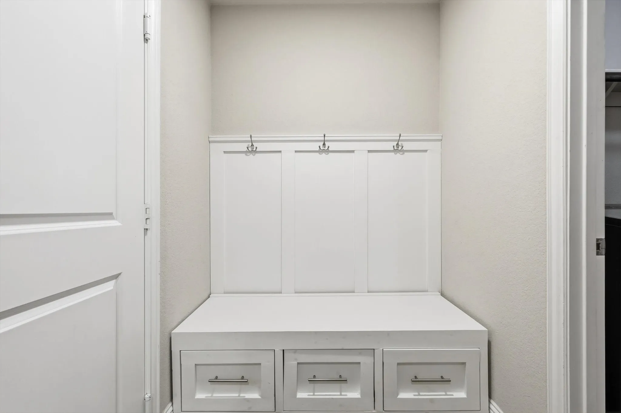 Built-in mudroom bench with three storage drawers, integrated coat hooks, and crisp white paneling