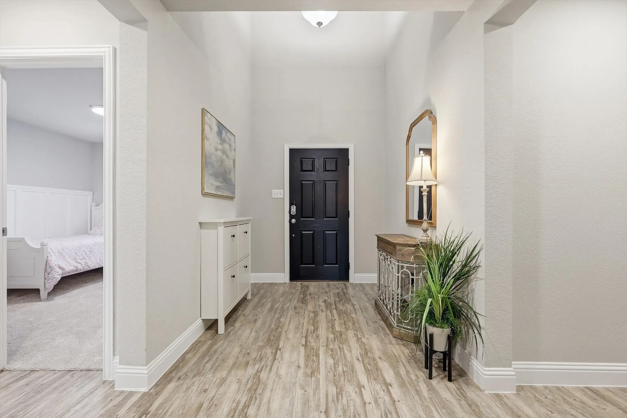Entryway featuring wood-finish flooring, a paneled black door, vaulted ceiling, and neutral wall tones