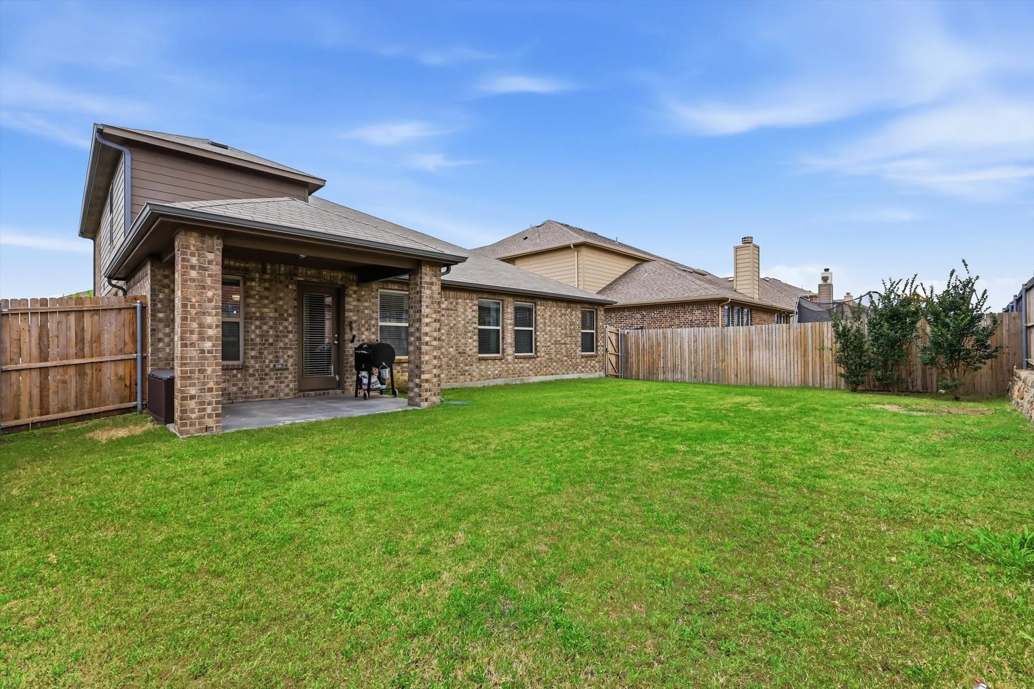 Expansive backyard featuring a covered patio with brick columns and a substantial lawn space.
