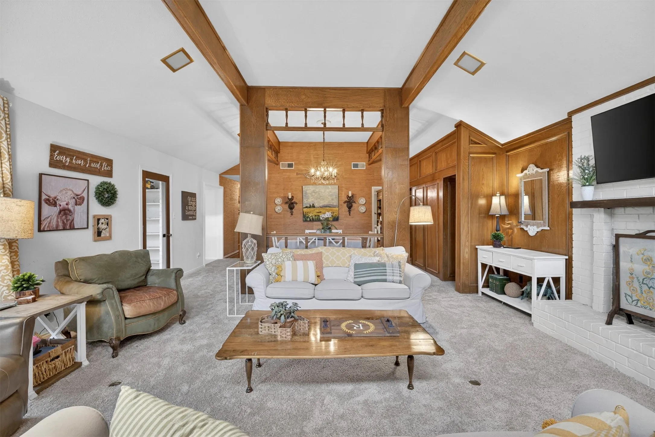 Expansive living area featuring light-colored carpeting, white painted walls, and wood-paneled accents