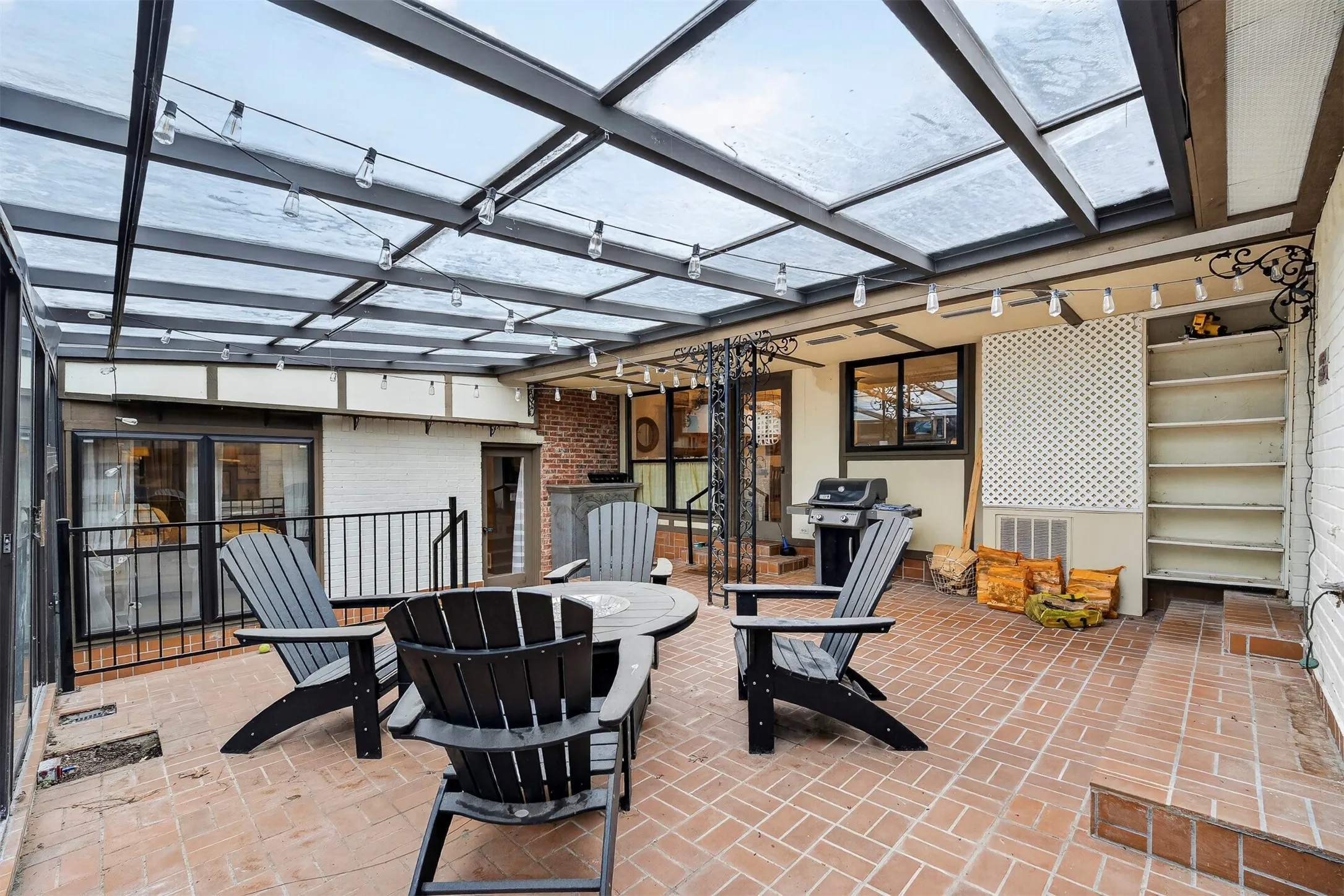 Brick patio featuring a transparent overhead covering, black metal framing, and built-in shelving