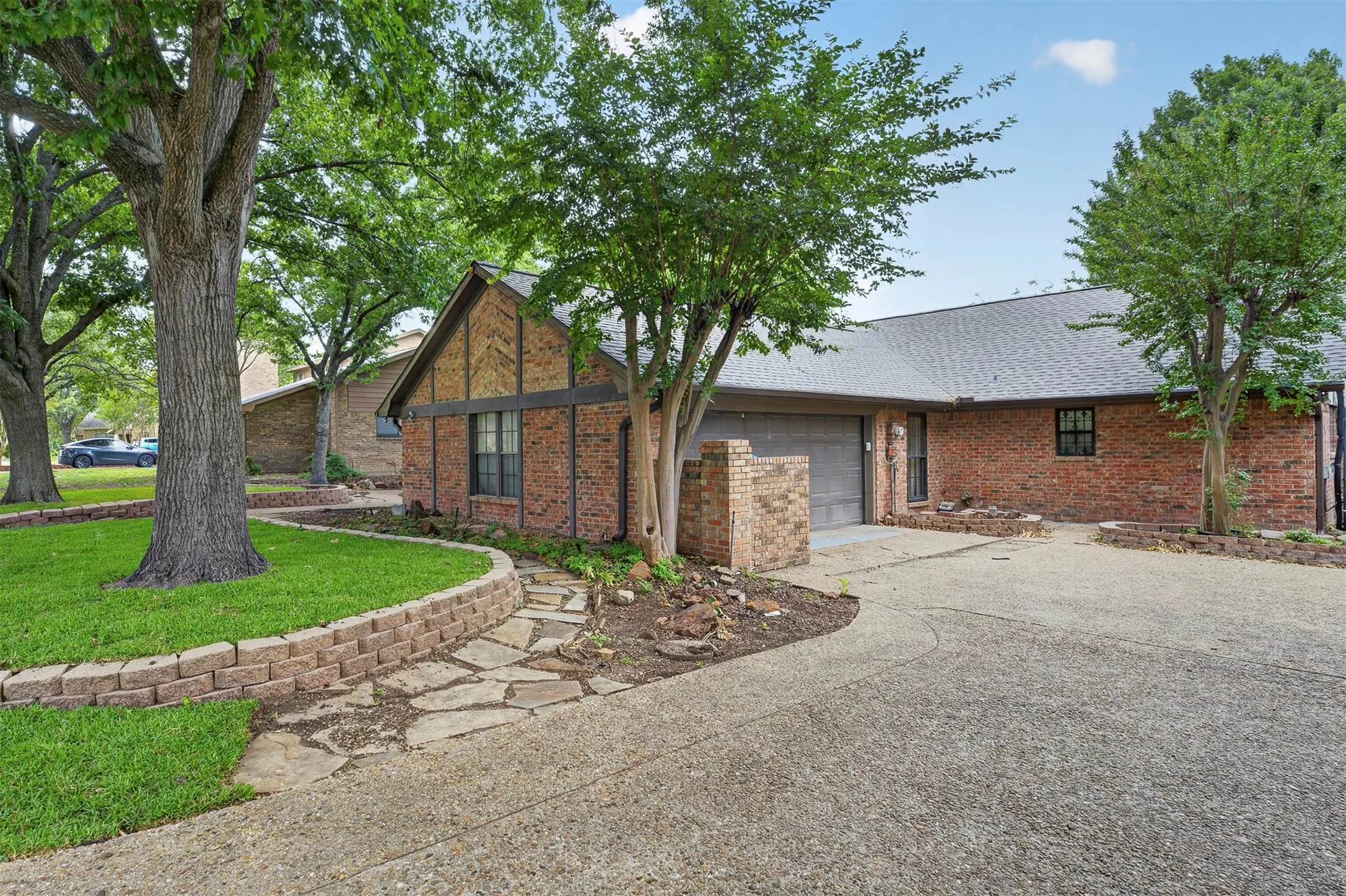 Brick exterior with a gabled roofline, concrete driveway, and a stone-paved walkway