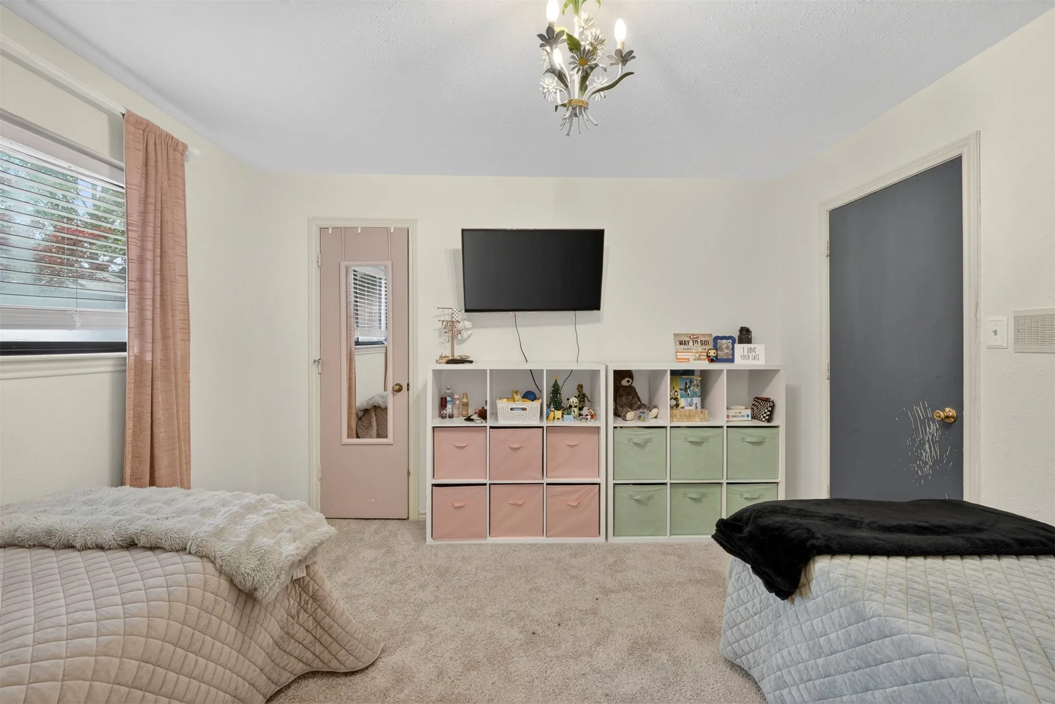 Carpeted interior space featuring white wall paint, a window with blinds and drapes, and a decorative ceiling light fixture