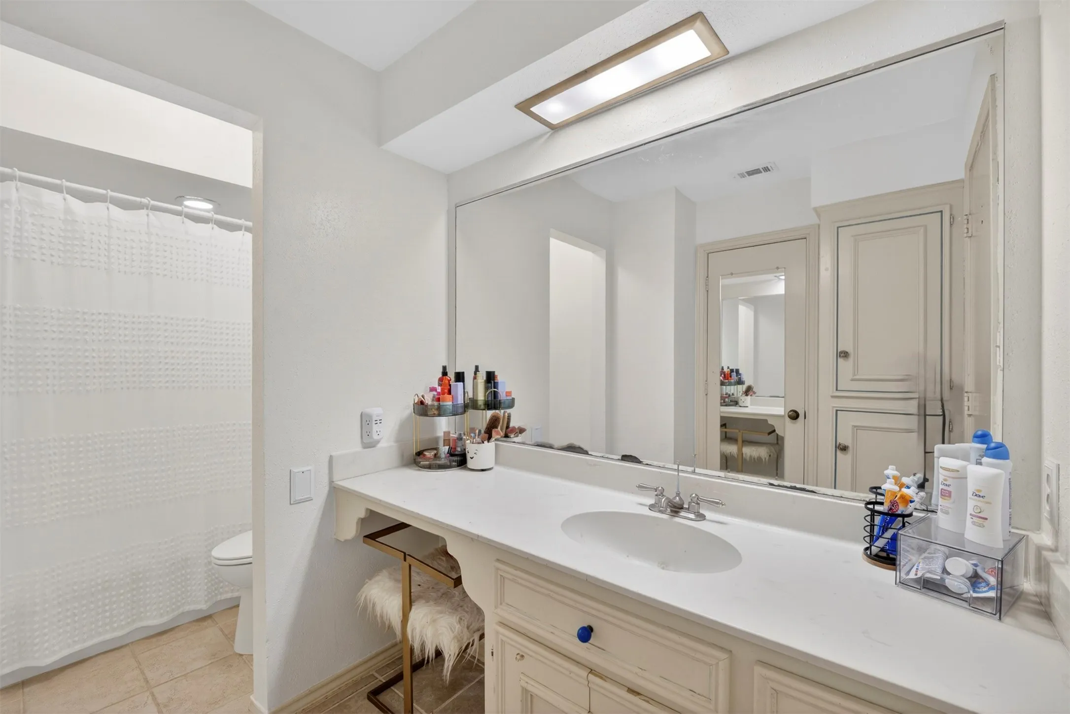 Bathroom featuring an integrated vanity with a single basin, a large wall-mounted mirror, and overhead lighting