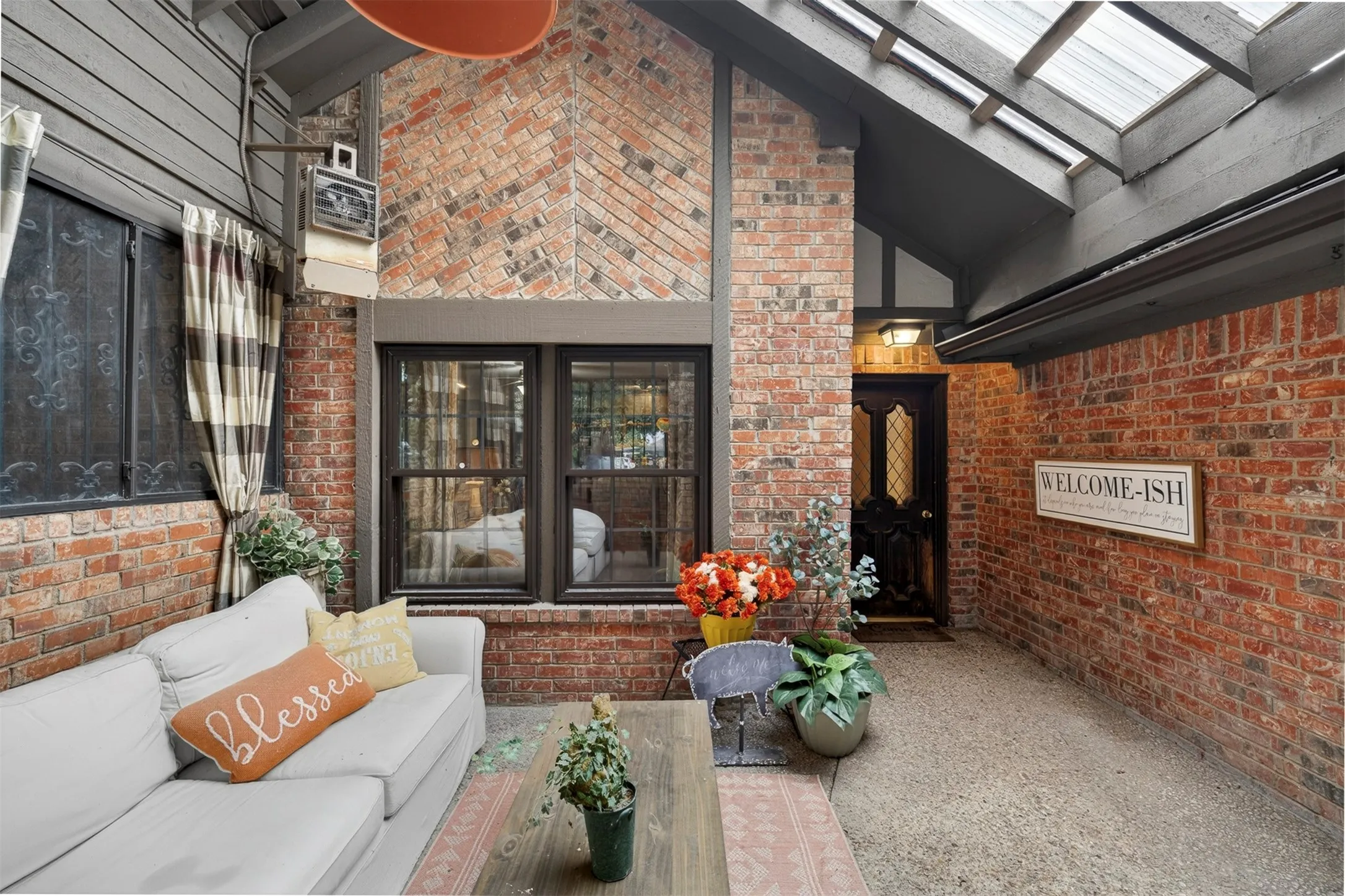 Covered patio featuring a brick accent wall, a glass-paneled entry door, a skylight roof, and two multi-pane windows