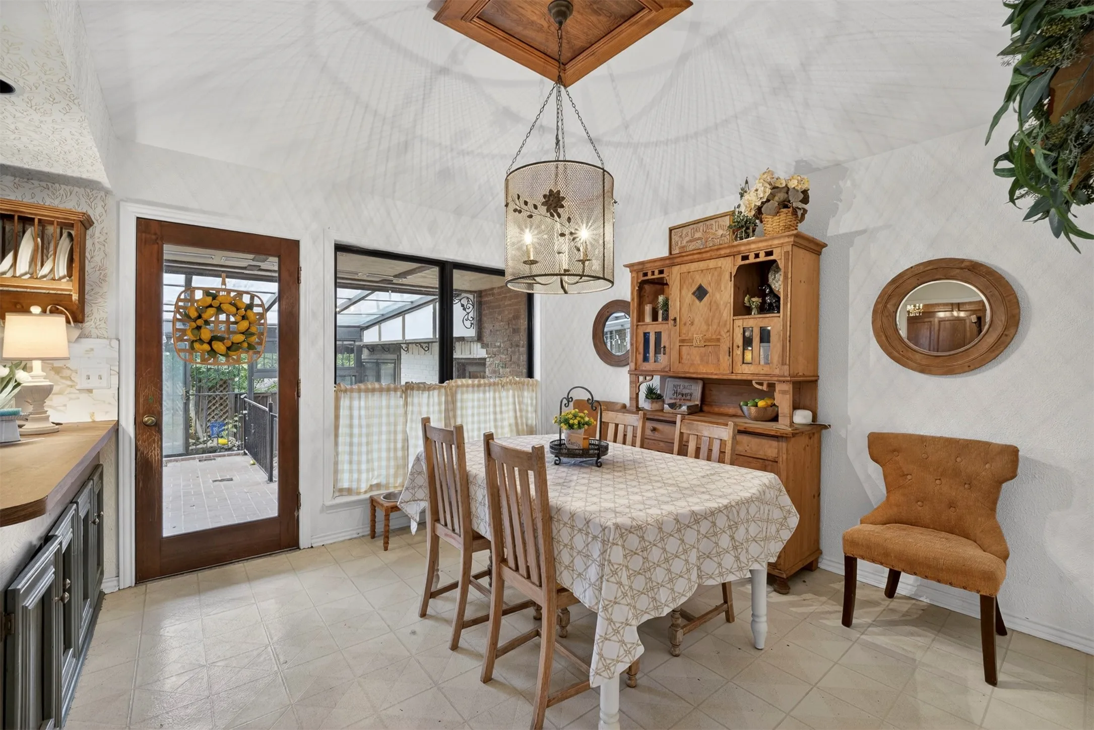 Spacious dining area featuring a decorative chandelier with an overhead wood ceiling accent, glass-paneled exterior door, and a built-in wood hutch