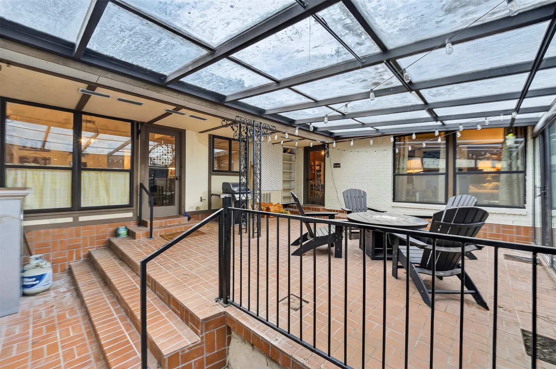 Covered brick patio featuring a transparent roof, black metal railing, and multiple windowed doors