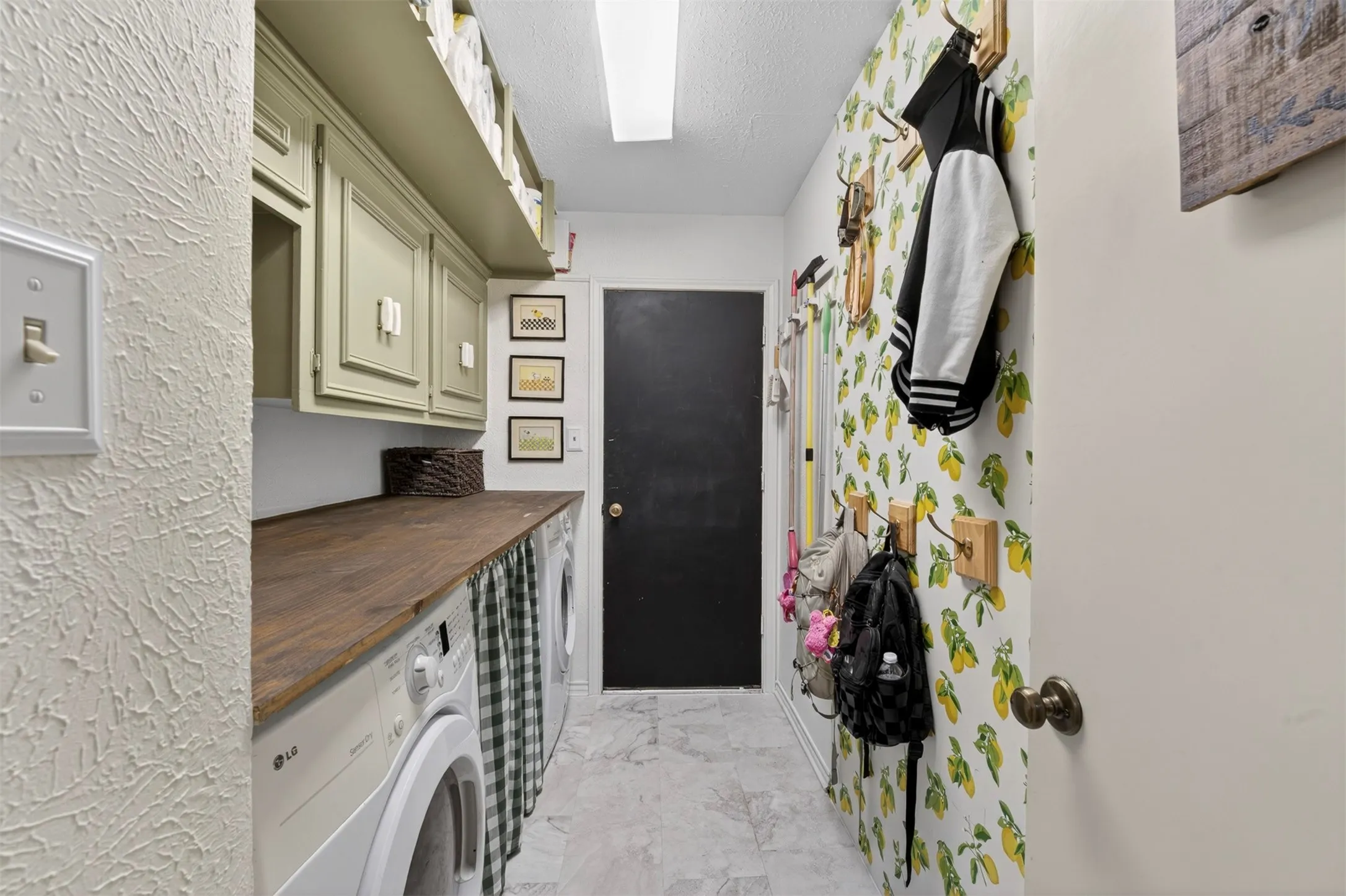 Utility room featuring a wood-finish countertop, upper cabinetry, and a patterned accent wall