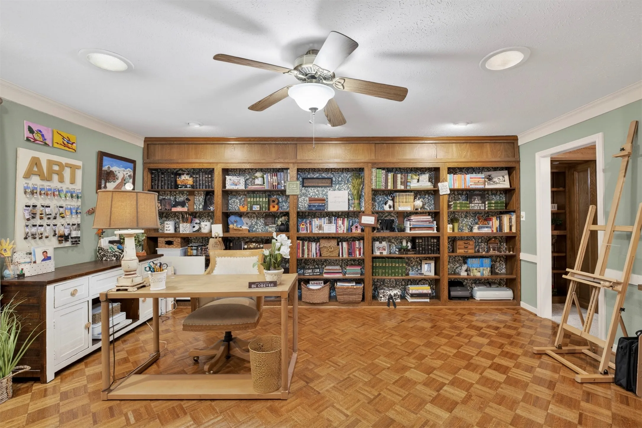 Rich wood-finish parquet flooring defines this versatile room featuring extensive built-in cabinetry, a ceiling fan, recessed lighting, and crown molding