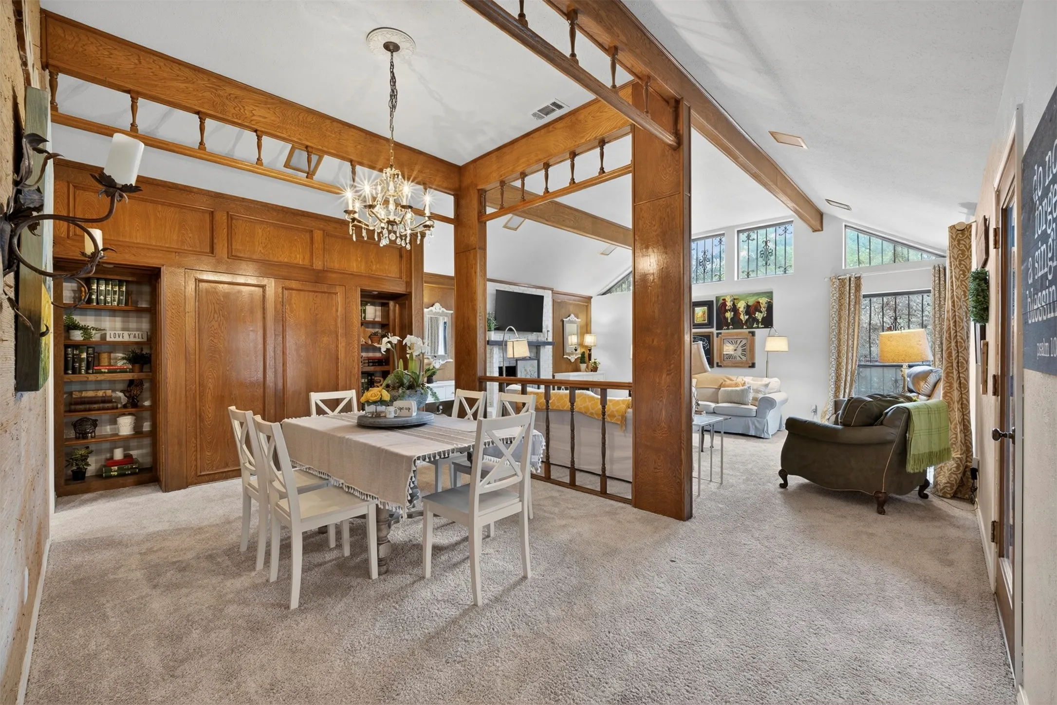 Open-concept dining and living areas featuring a vaulted ceiling with exposed wood beams, recessed wall shelving, and a chandelier