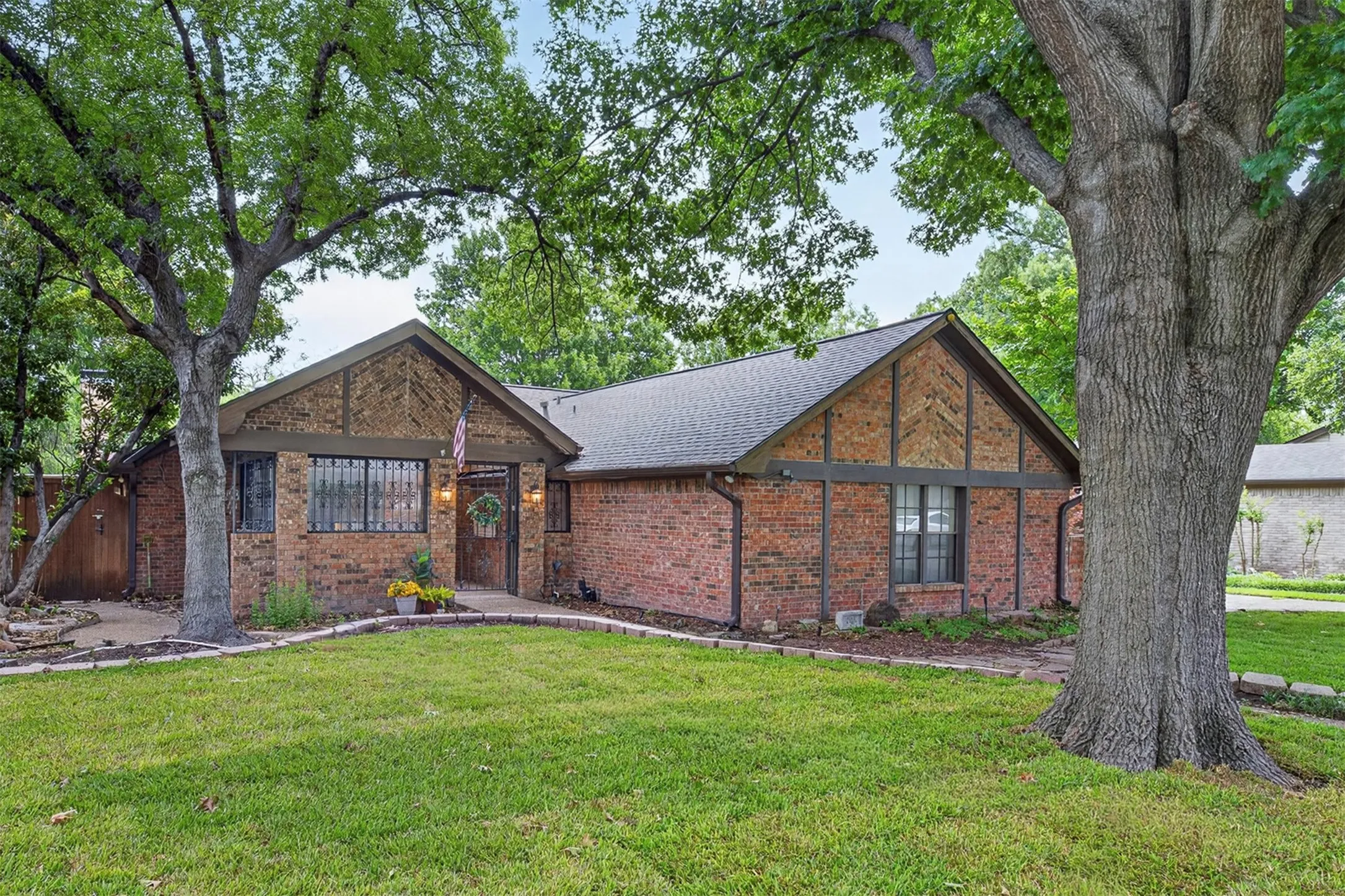 Brick exterior with patterned gable accents, mature tree canopy, front entry with transom window, and a gabled roofline