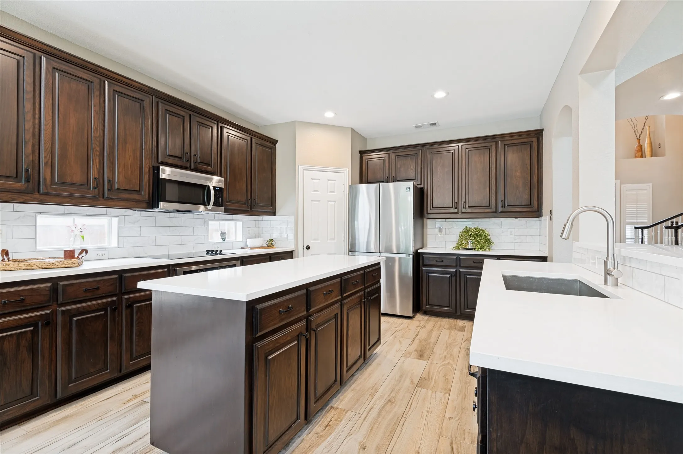 Kitchen featuring dark wood cabinetry, stainless steel appliances, a white subway tile backsplash, light countertops, and wood-finish flooring