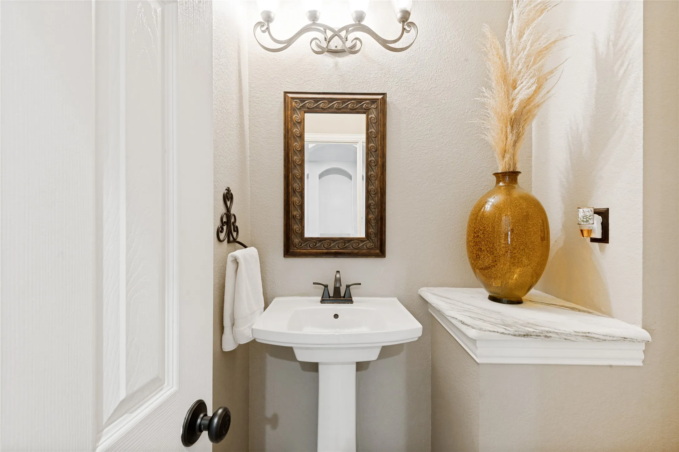 Pedestal sink with black faucet, framed mirror, and wall-mounted vanity lighting