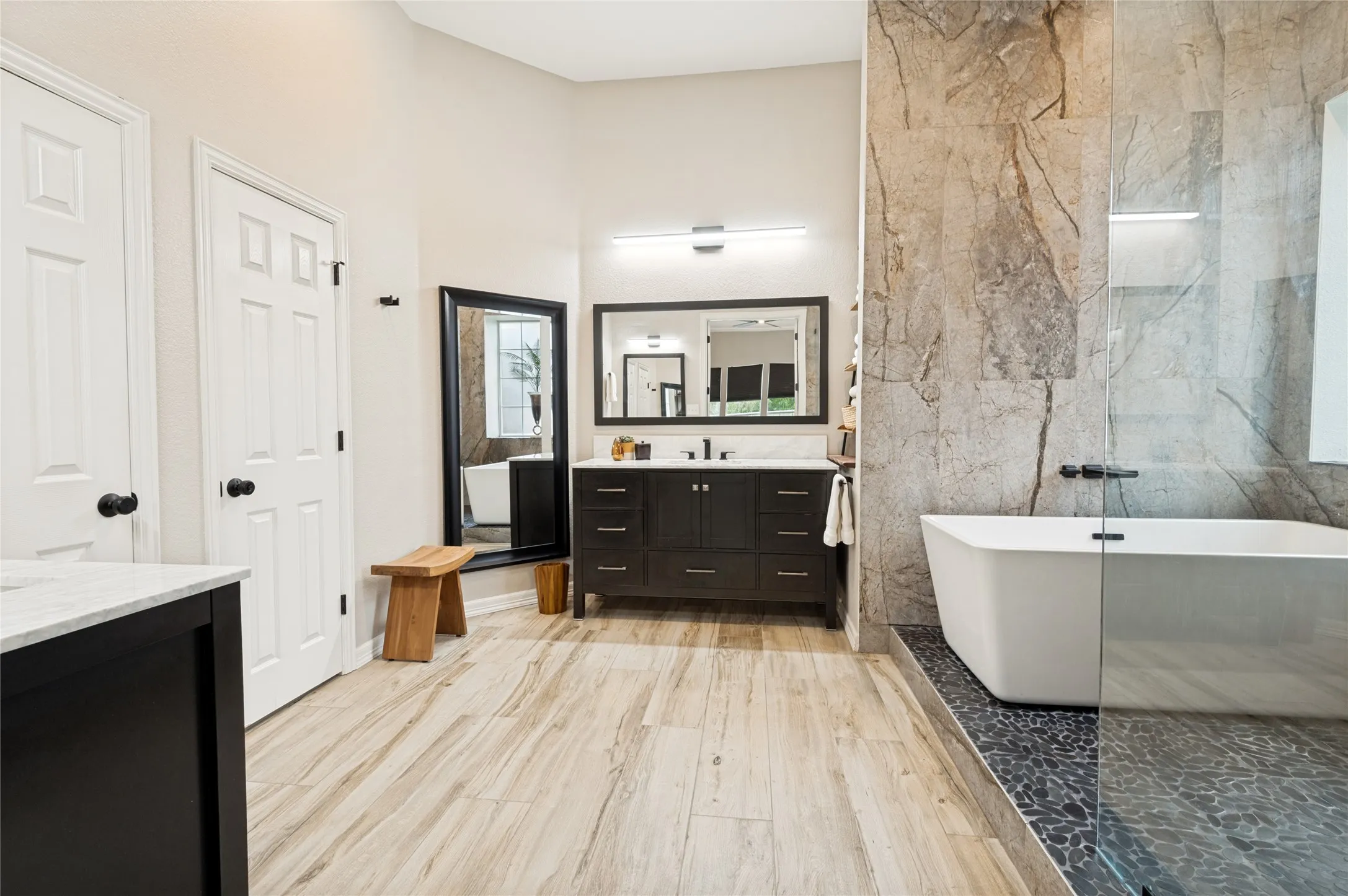 Contemporary bathroom featuring a freestanding tub, a walk-in shower with a glass enclosure, a dark wood-finish vanity with a double sink, and wood-look tile flooring