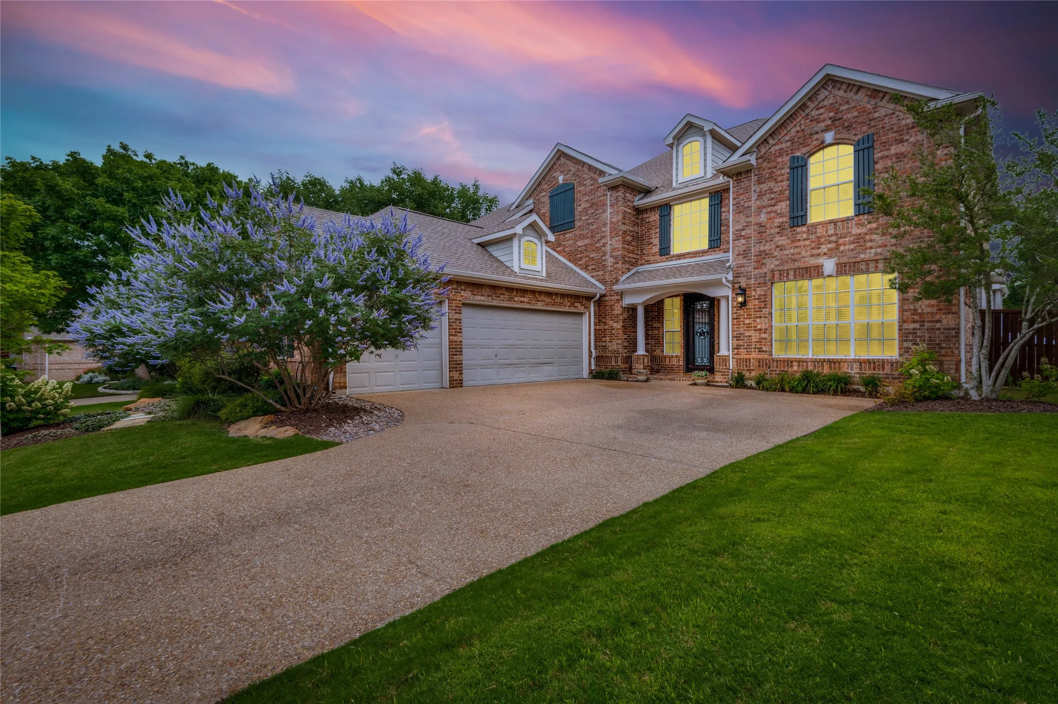 Brick exterior with multiple dormer windows, a three-car garage, and an exposed aggregate driveway
