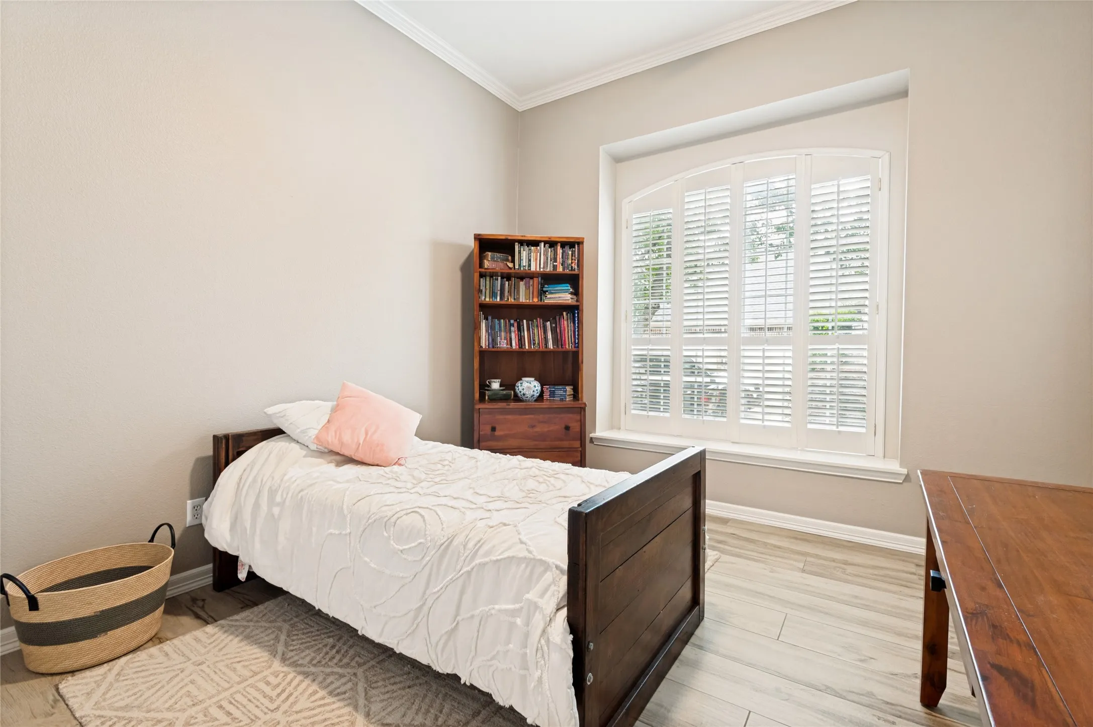 Arched window with plantation shutters, light wood-finish flooring, crown molding, and neutral wall tones
