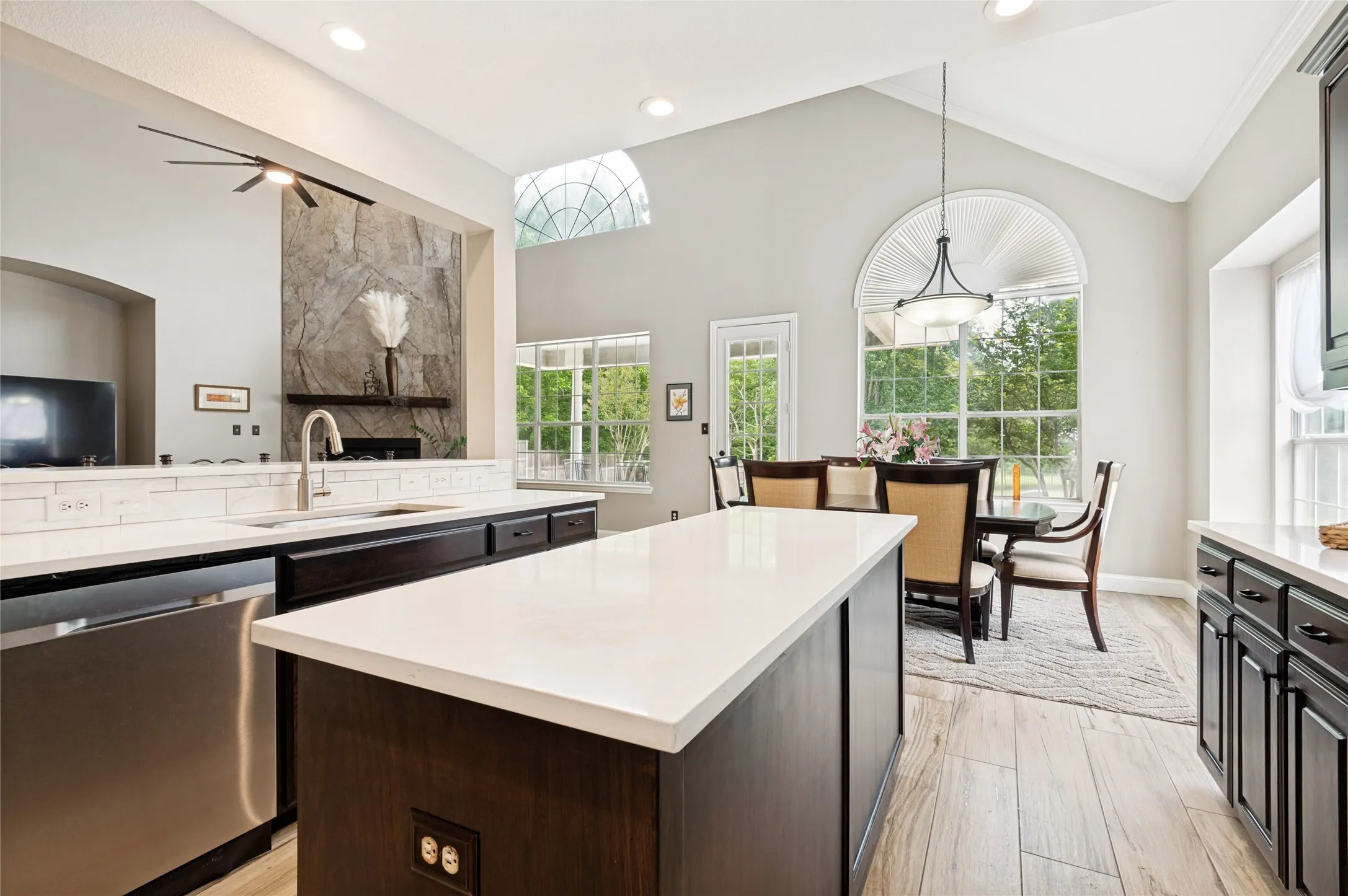 Open-concept kitchen featuring a large central island with light-toned countertops, dark wood cabinetry, and wood-finish flooring