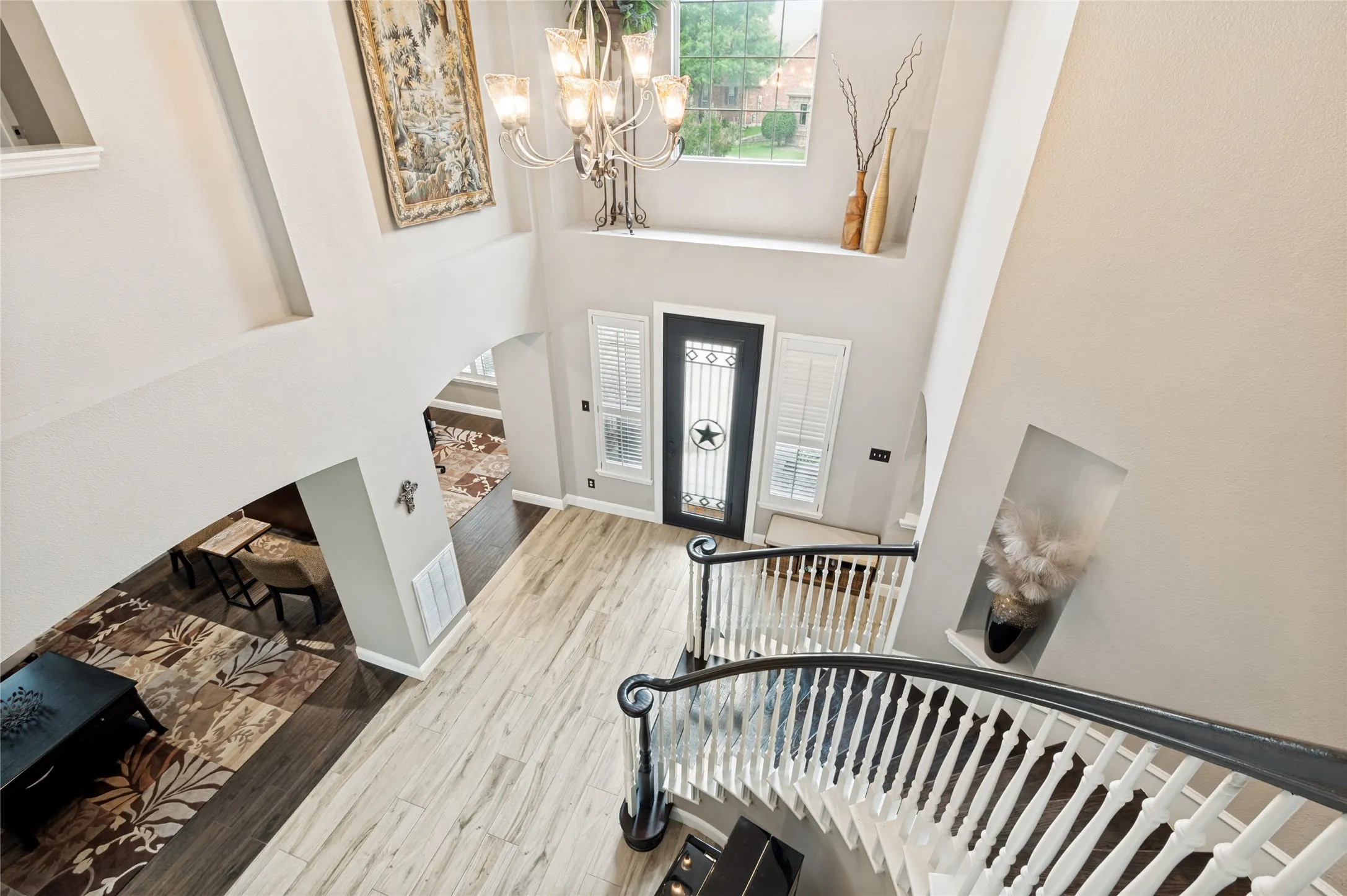 Two-story foyer featuring a curved staircase with dark wood handrails and white balusters, light wood-finish flooring, and a decorative chandelier
