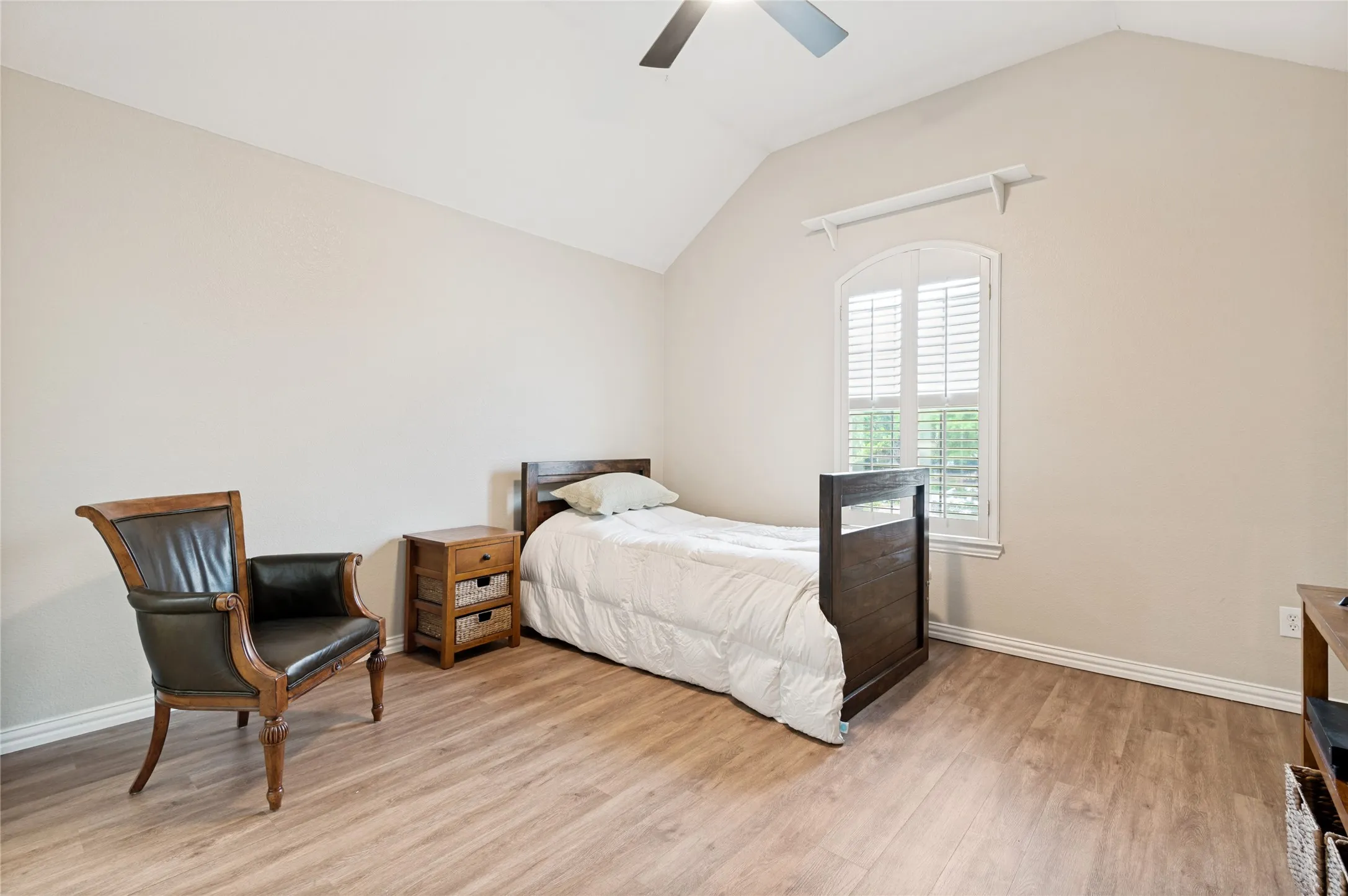 Spacious room featuring vaulted ceilings, wood-finish flooring, a contemporary ceiling fan, and an arched window with plantation shutters