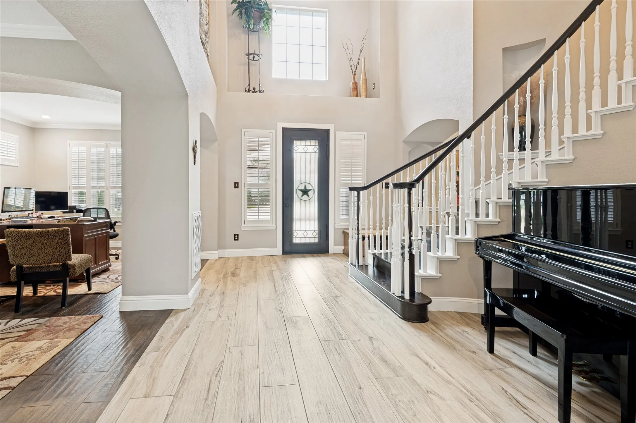 Two-story foyer featuring wood-finish flooring, a dark entry door with decorative glass, and a grand staircase with white spindles and a dark handrail