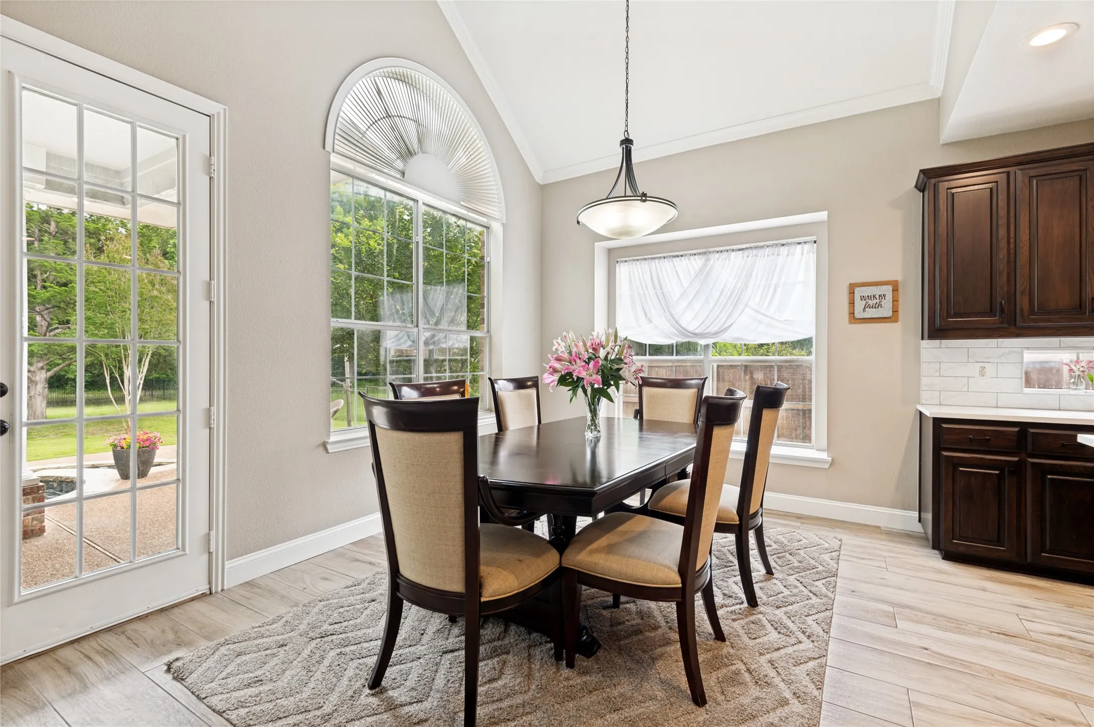 Vaulted ceiling dining area featuring a large arched window, a glass-paned exterior door, wood-finish flooring, and crown molding