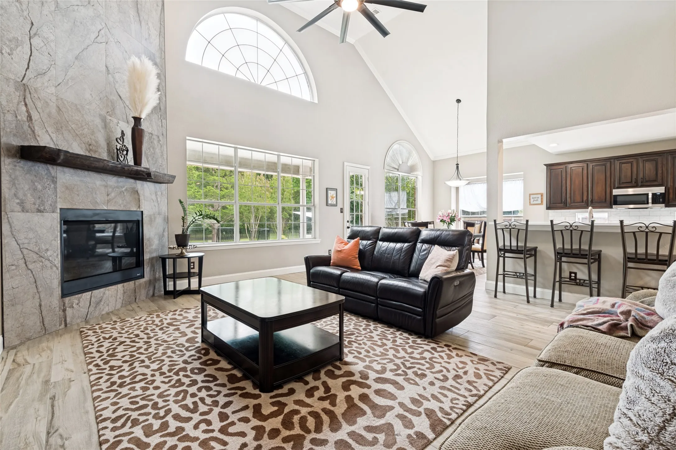 Living area featuring a stone-clad fireplace with a timber mantel, vaulted ceilings, and large windows