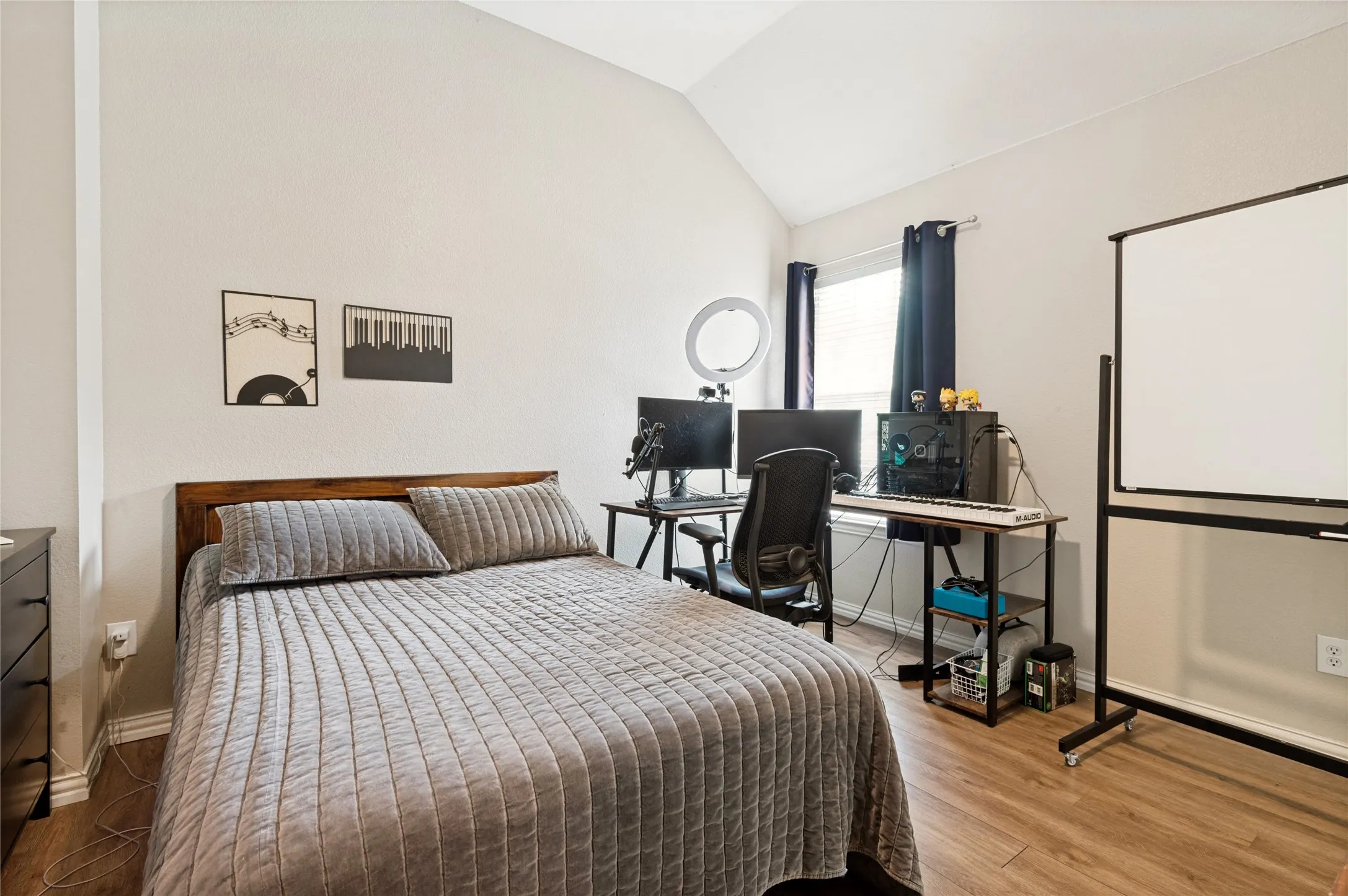 Vaulted ceiling bedroom featuring wood-finish flooring, a window with blinds, and light-toned walls