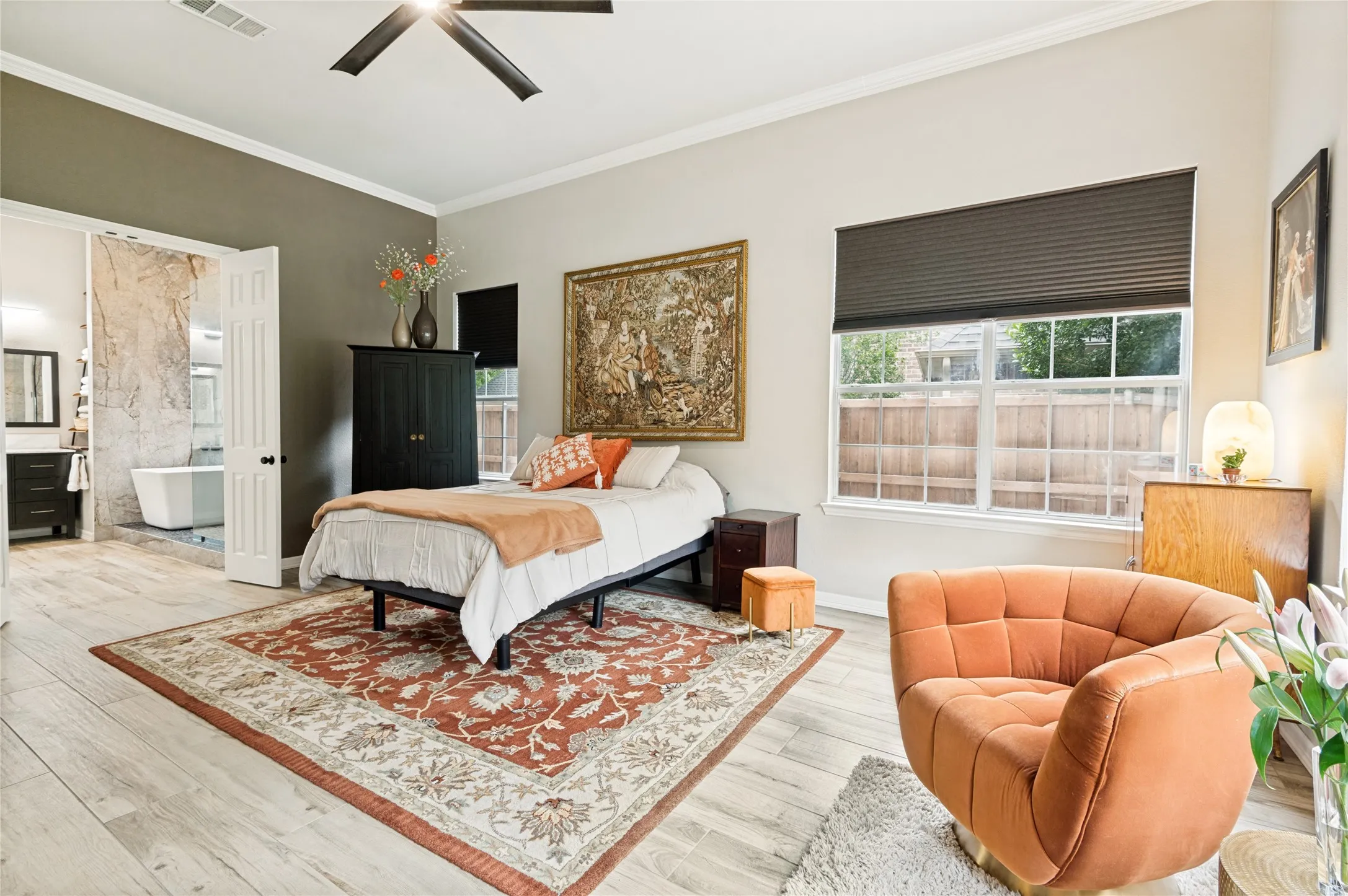 Spacious bedroom featuring light-toned wood-finish flooring, a ceiling fan, and a large window with privacy blinds