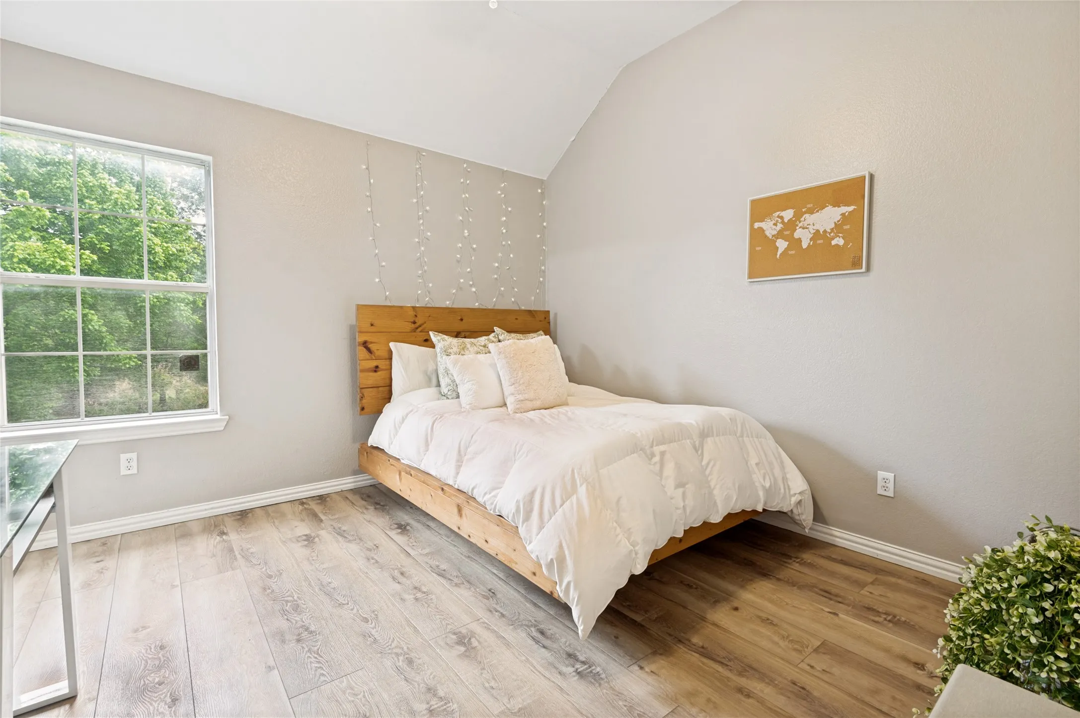 Vaulted ceiling bedroom featuring wood-finish flooring, a large multi-pane window, and light-toned walls