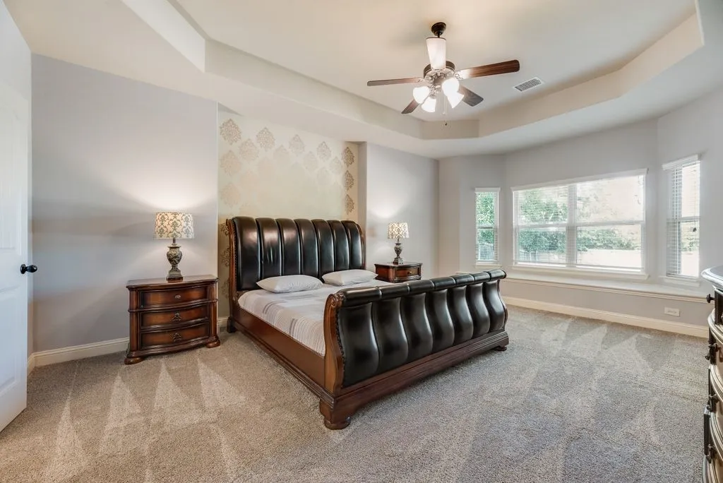 Spacious bedroom featuring a tray ceiling with a ceiling fan