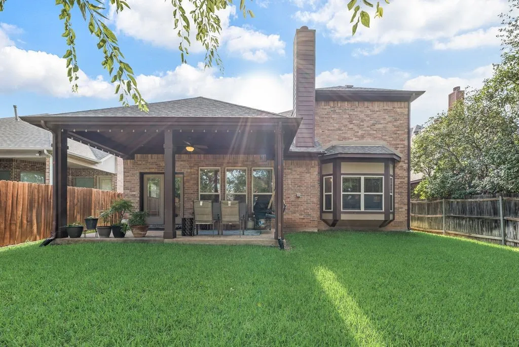 Expansive green lawn with a covered patio featuring a ceiling fan and string lights