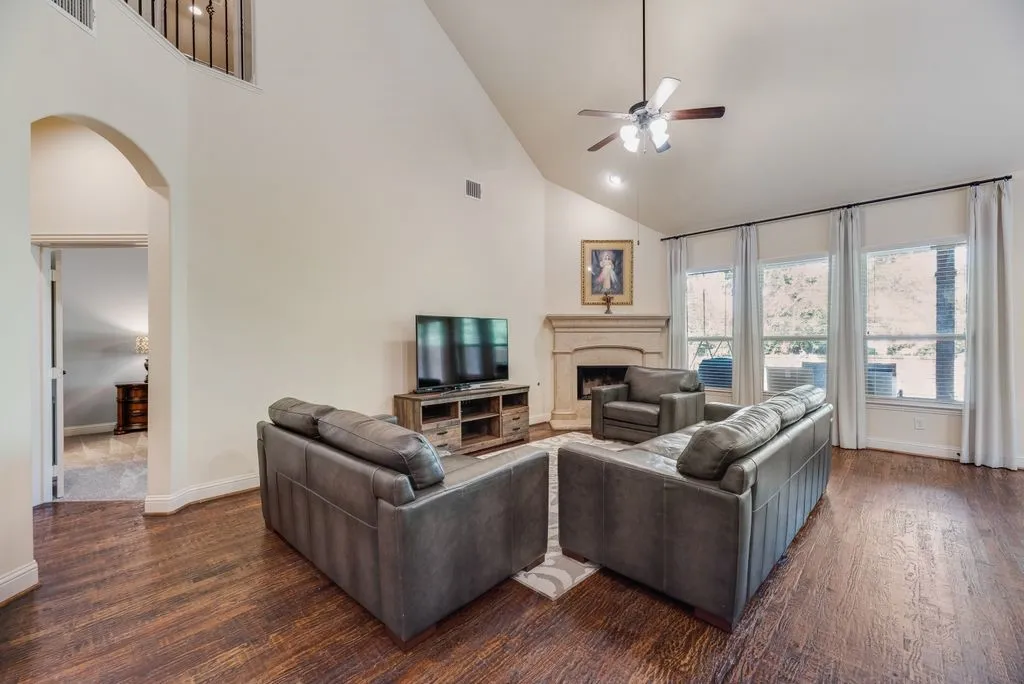 Vaulted ceiling living area featuring rich wood-finish flooring, a decorative stone fireplace, recessed lighting, and a ceiling fan