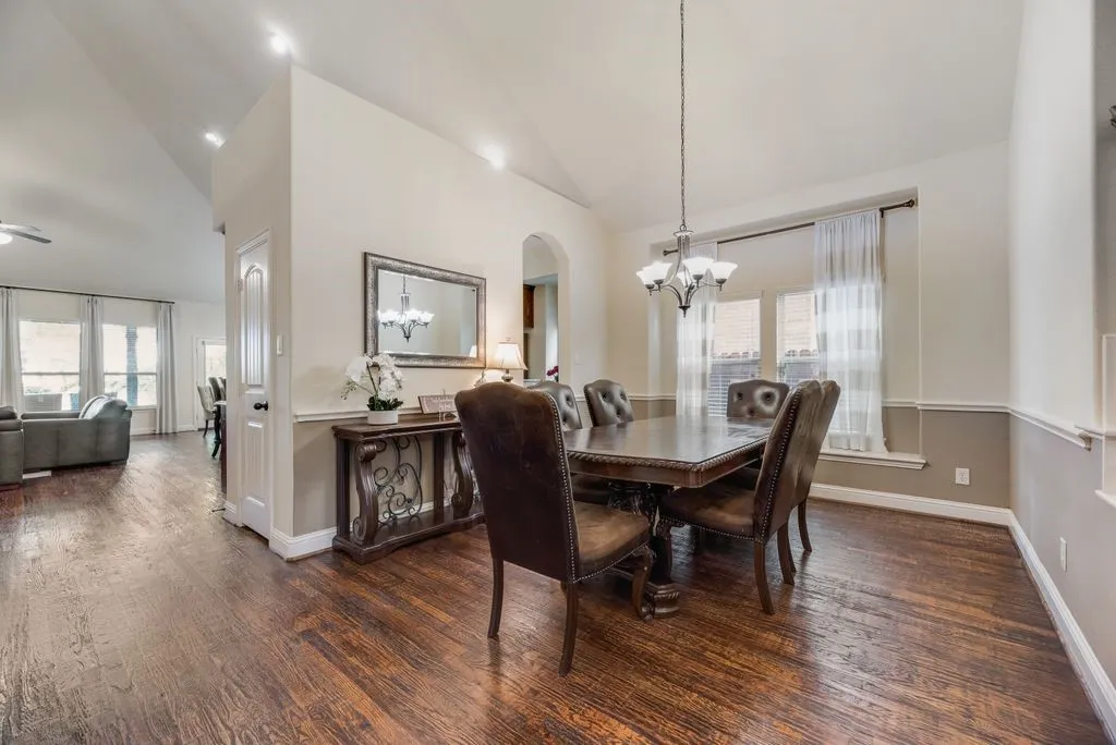 Dining area featuring wood-finish flooring, a contemporary chandelier, multiple windows with white sheer curtains, and two-tone wall paneling