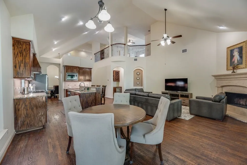Open-concept living area with vaulted ceilings, dark wood-finish flooring, a kitchen island with seating, a stone fireplace, and a second-story balcony overlooking the space