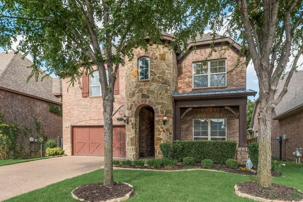 Brick and stone exterior featuring an arched entryway, covered porch, and a two-car garage with double doors