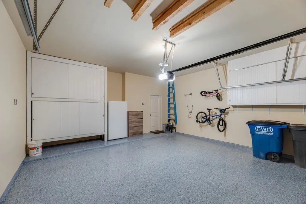 Garage with speckled epoxy flooring, overhead garage door opener, built-in wall cabinetry, and exposed ceiling joists