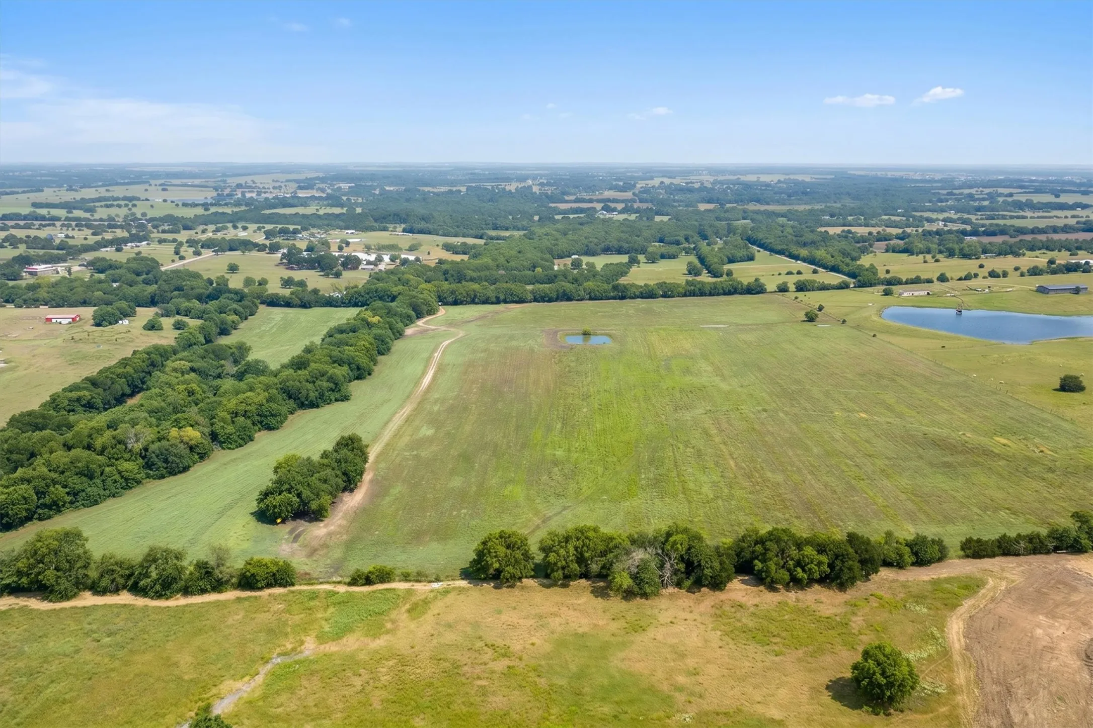 Expansive rural landscape featuring cleared land, scattered trees, and two distinct water features