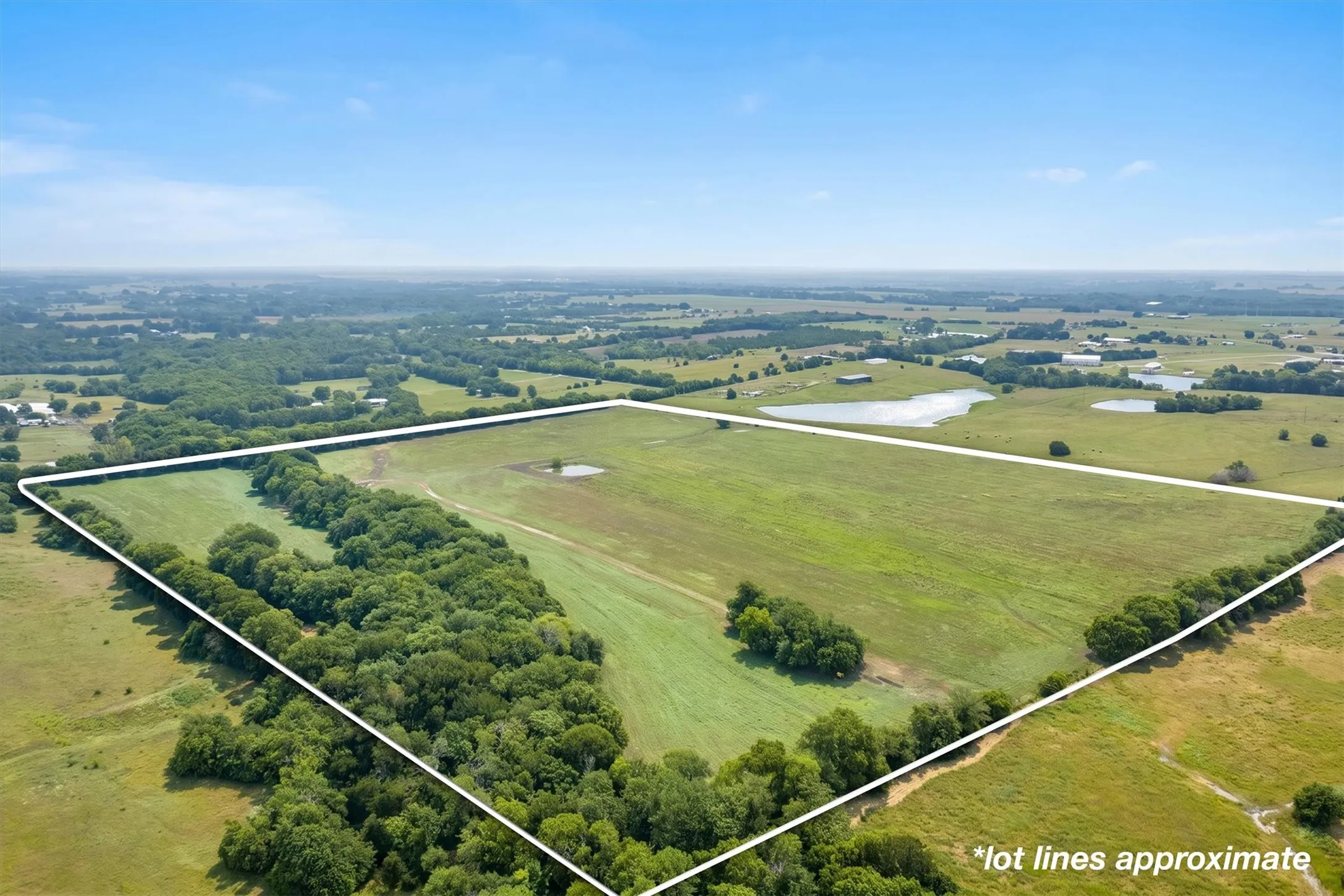Expansive land parcel featuring open fields, natural tree lines, and a visible pond