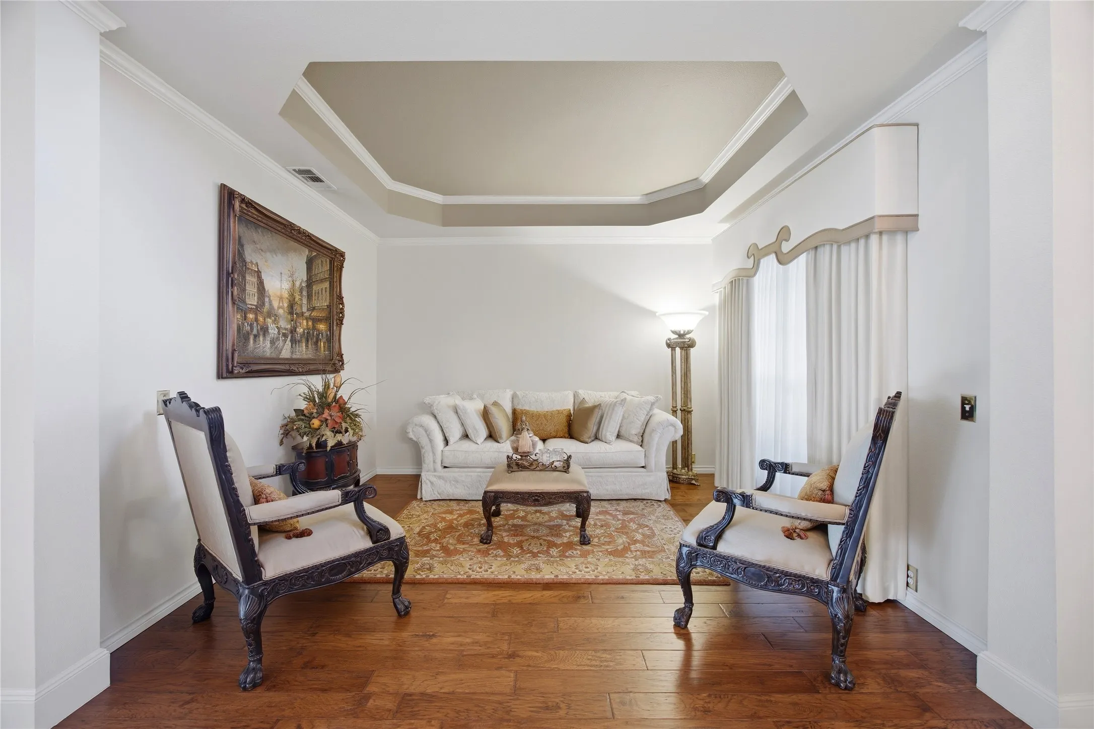Living area featuring wood-finish flooring, a tray ceiling with crown molding, and white walls