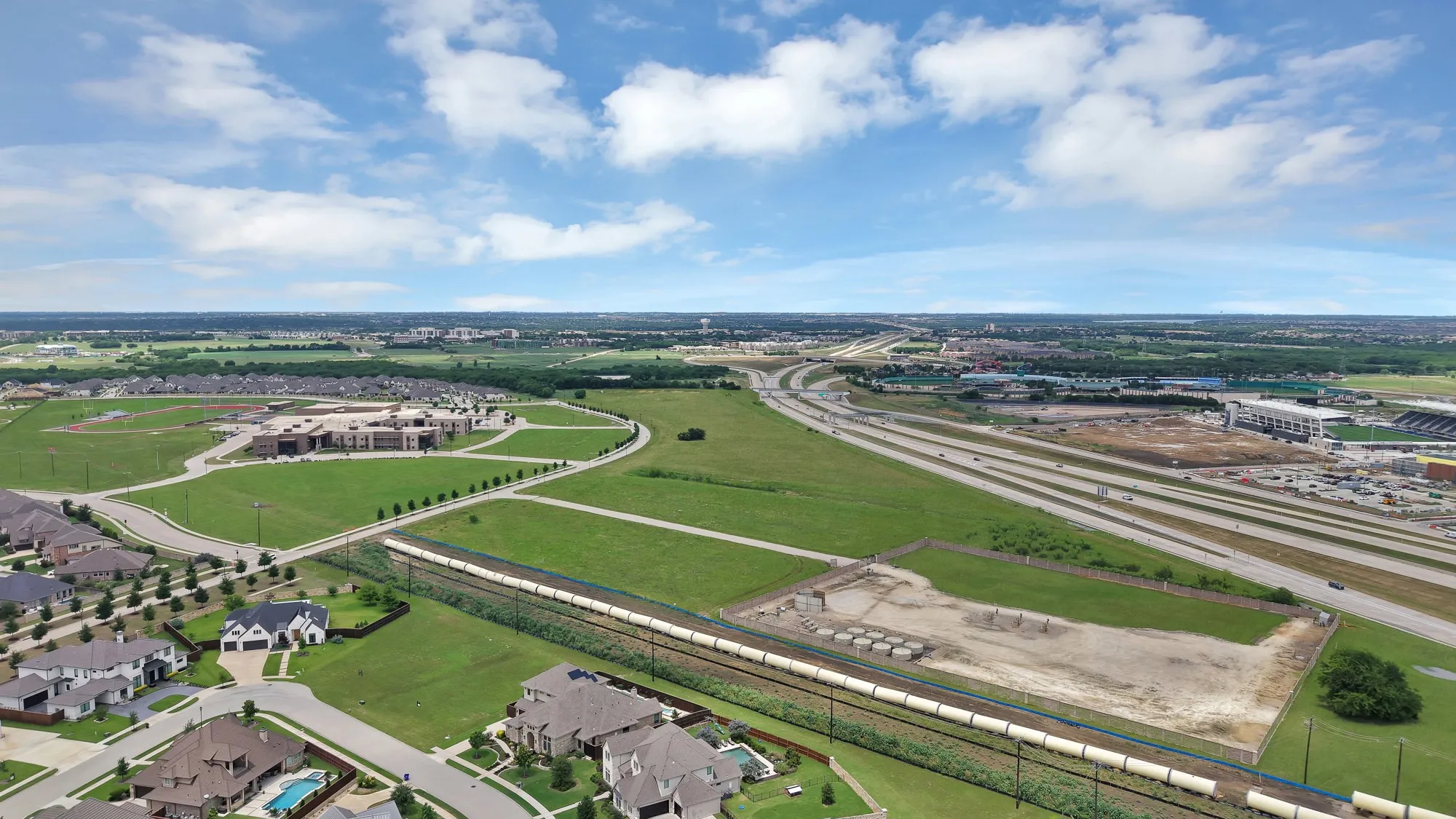 Community context and highway access — Aerial view showing proximity to major highway interchange, school campus, and surrounding master-planned development. Dense tree canopy and open land buffers to the north.