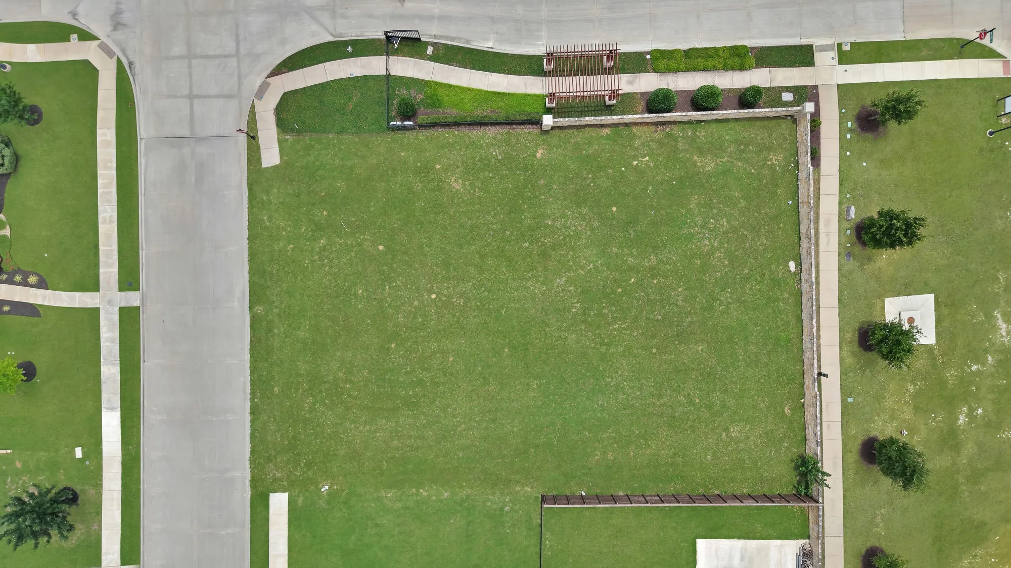 Lot aerial top-down — Level, rectangular lot with existing sidewalk and gated community wall along the north boundary. Concrete driveway stub and curb cut in place at street.