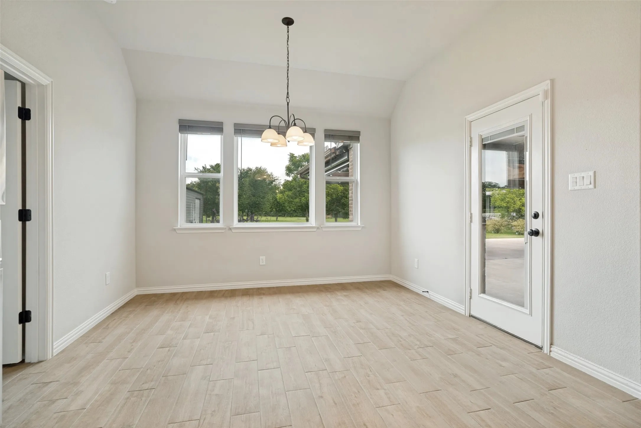 Dining area featuring wood-finish flooring, vaulted ceiling, and a three-light chandelier