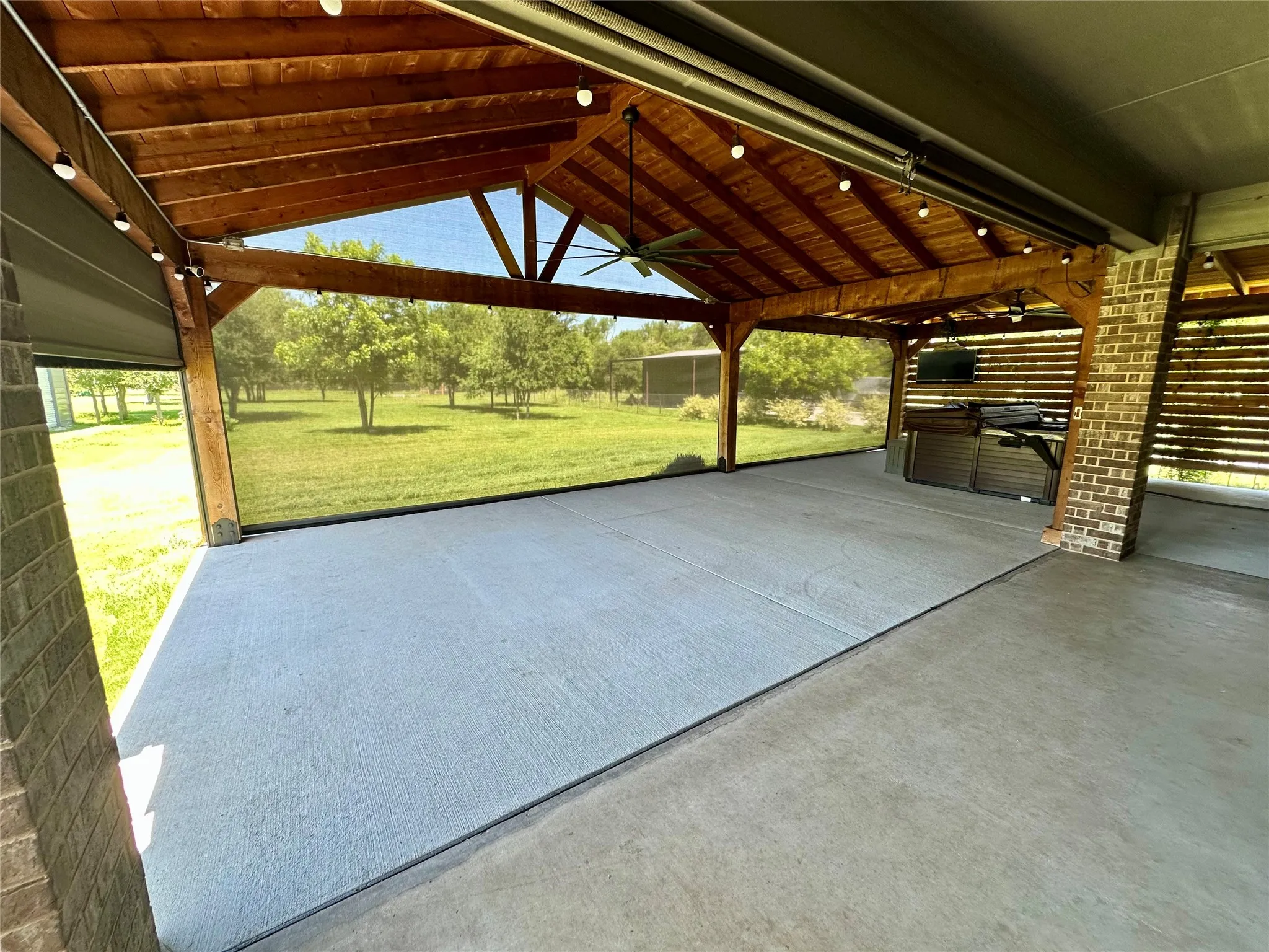 Spacious covered patio featuring a concrete surface, exposed wood beam ceiling, string lighting, and a ceiling fan