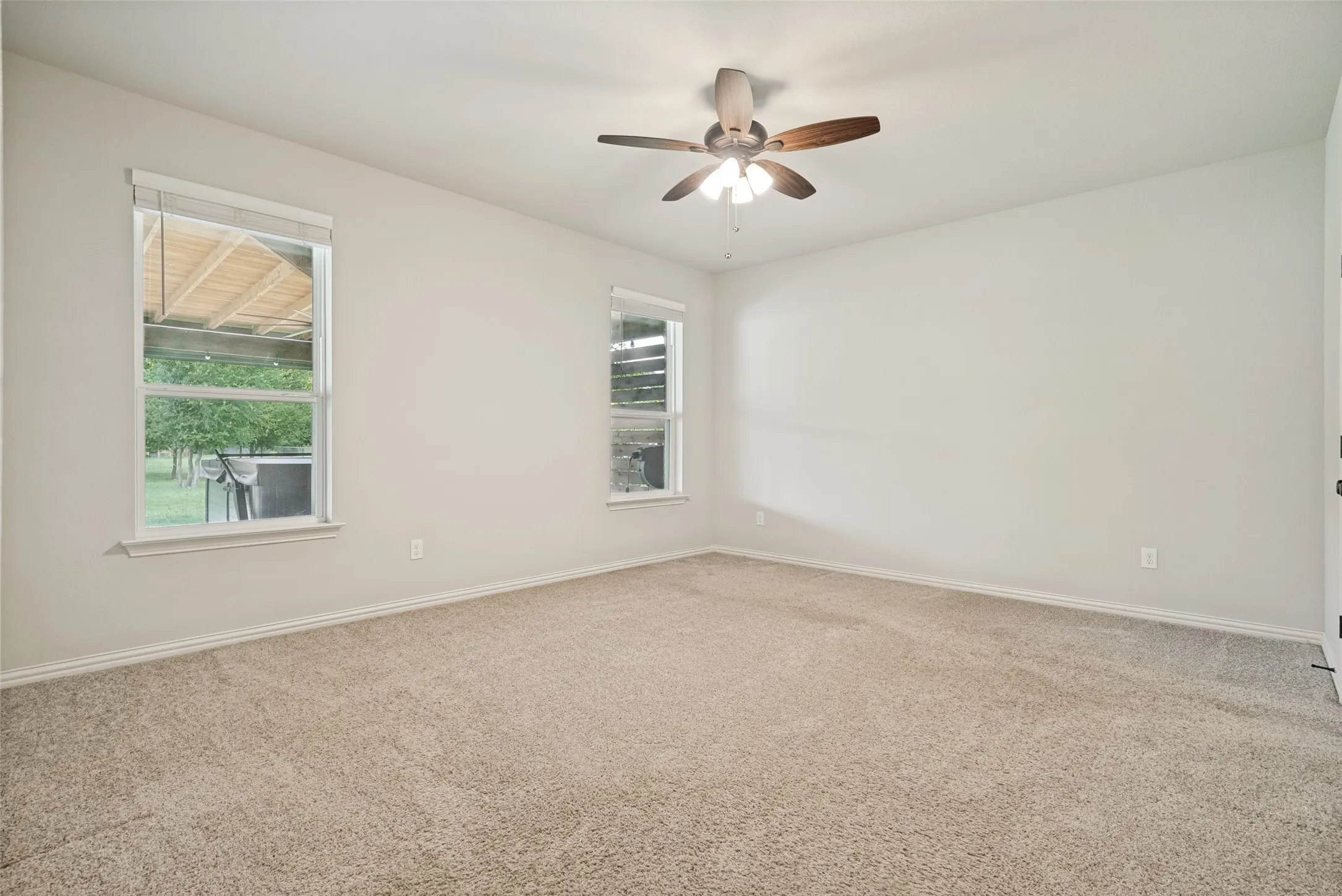 Spacious room featuring neutral carpeting, light-toned walls, and a ceiling fan with light fixture