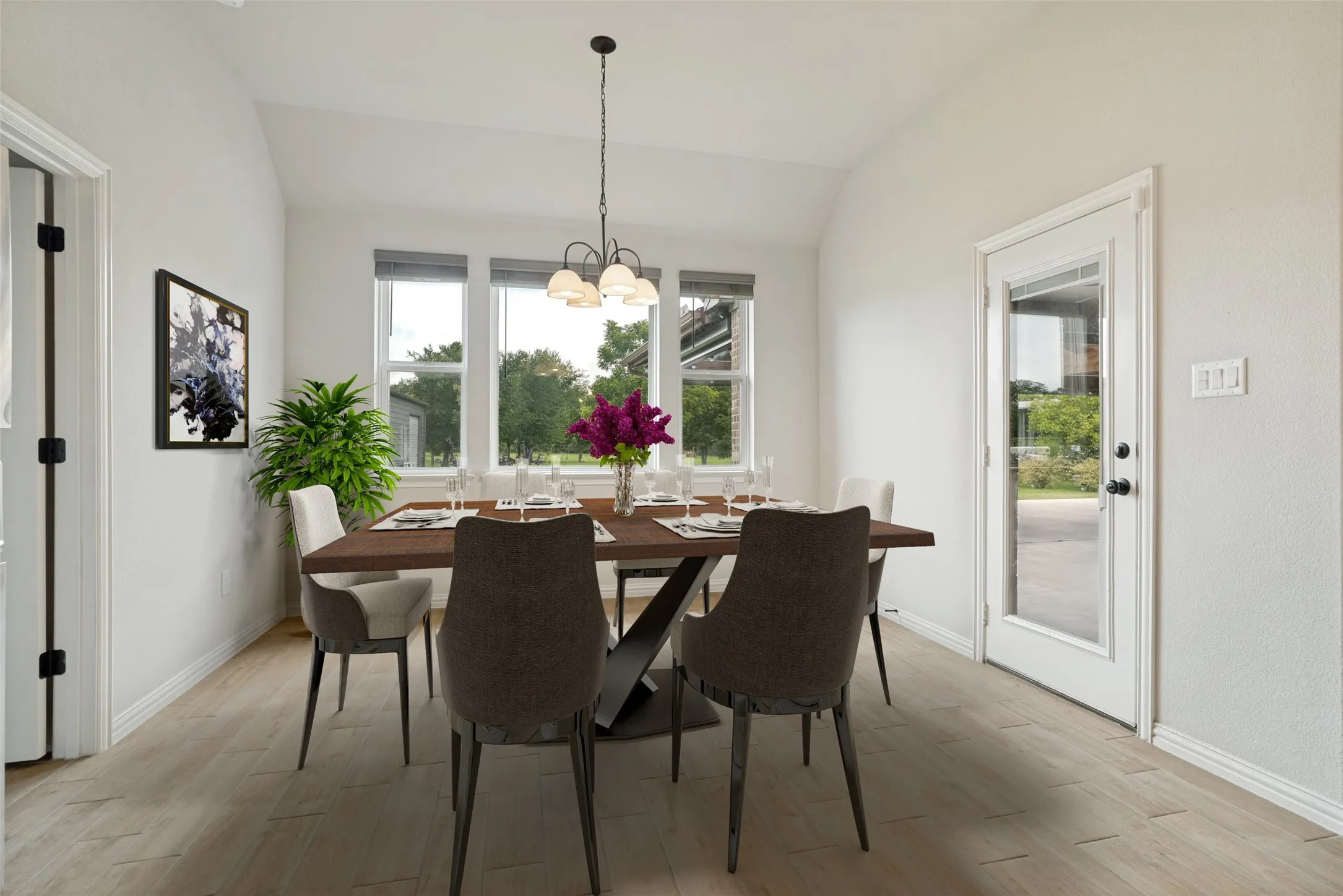 Vaulted ceiling dining area featuring wood-finish flooring, a three-window wall, an exterior glass-paneled door, and a multi-bulb chandelier