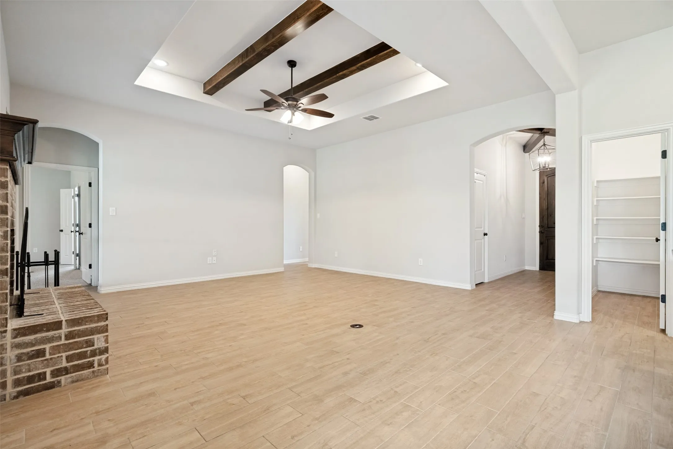 Spacious interior featuring wood-finish flooring, a tray ceiling with exposed wood beams, a ceiling fan, and an arched doorway