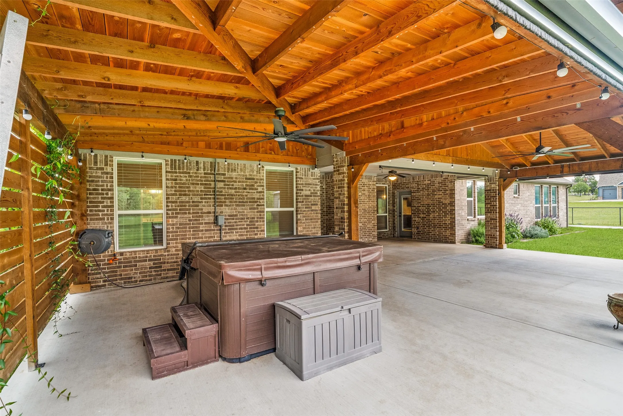 Expansive covered patio featuring a natural wood ceiling, exposed beams, multiple ceiling fans and remote screens to enclose