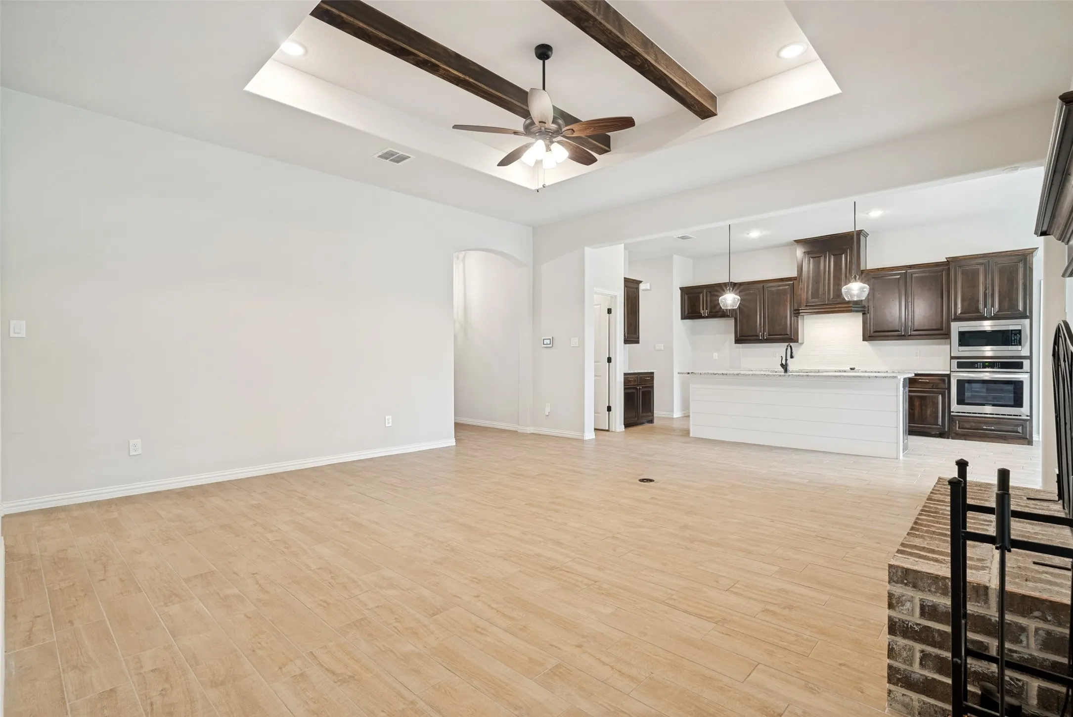 Open-concept living area with wood-finish tile flooring and a tray ceiling featuring decorative wood beams and a ceiling fan